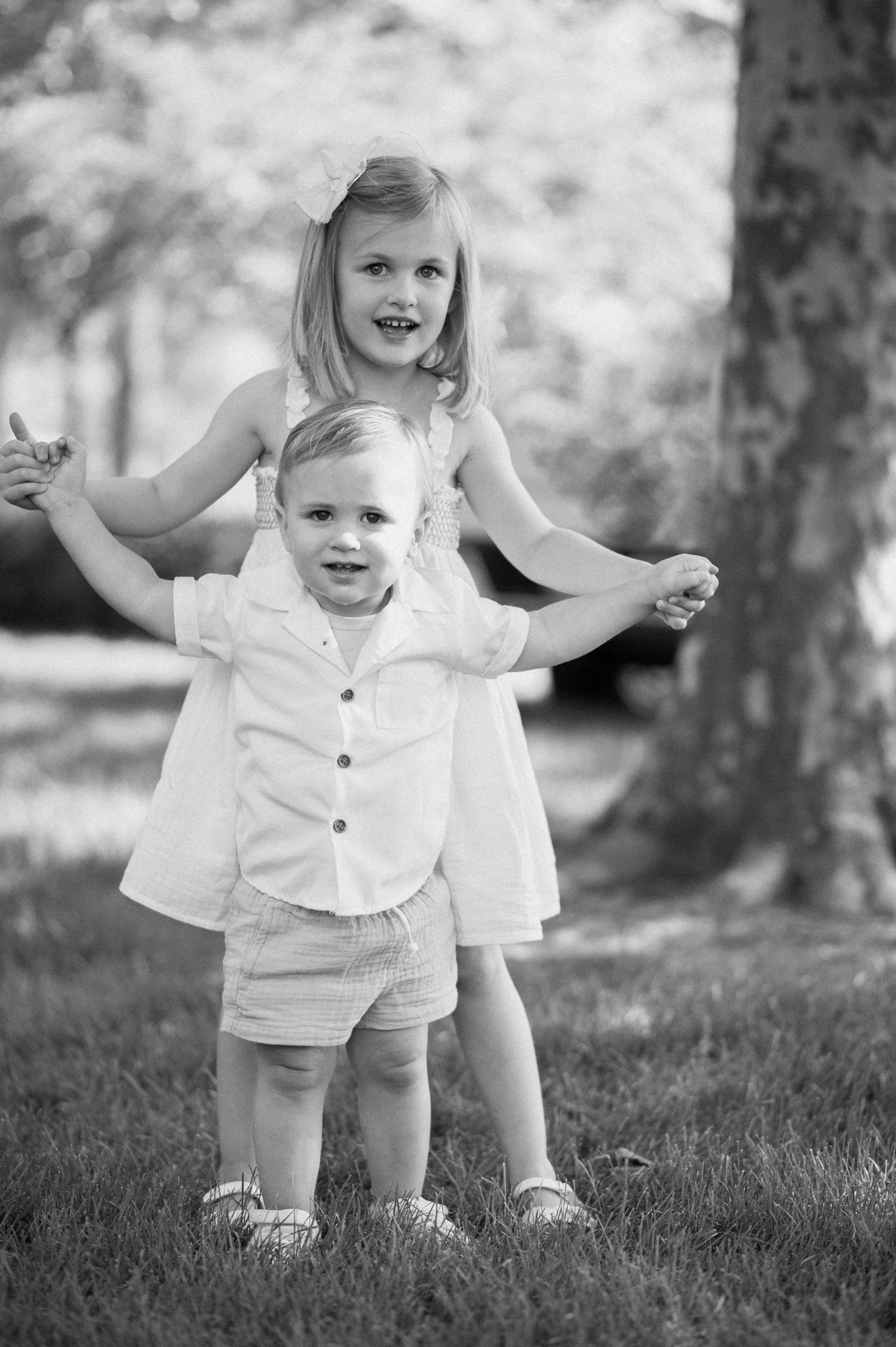 Black and white photo of toddler learning to walk outdoors.