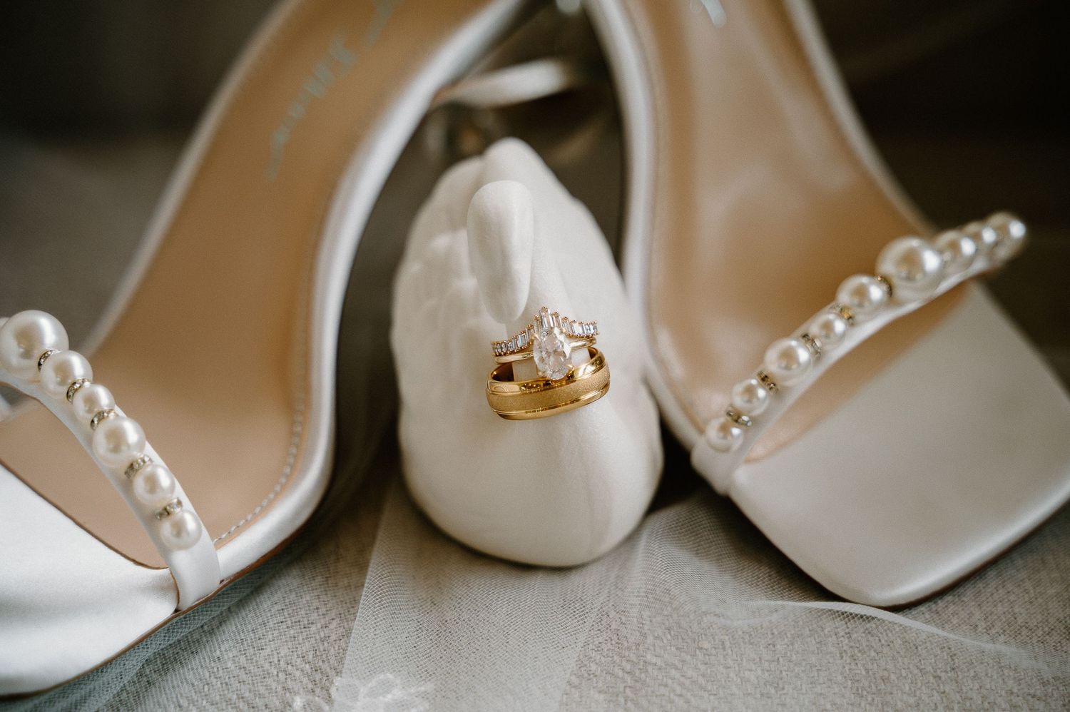 White pearl-embellished bridal heels with gold wedding bands and diamond engagement ring displayed elegantly.