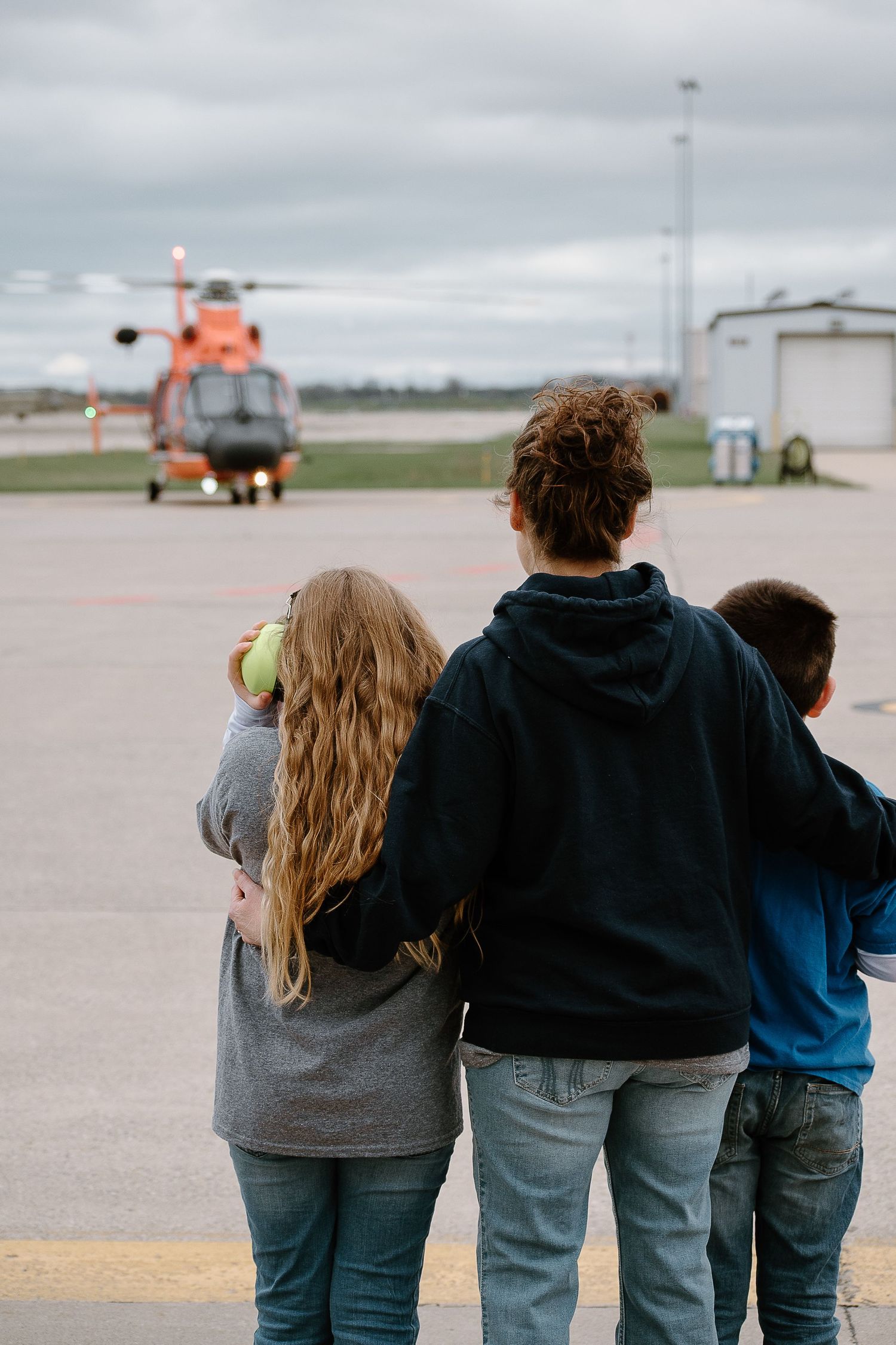 Group of people standing together watching aircraft on runway at distance.