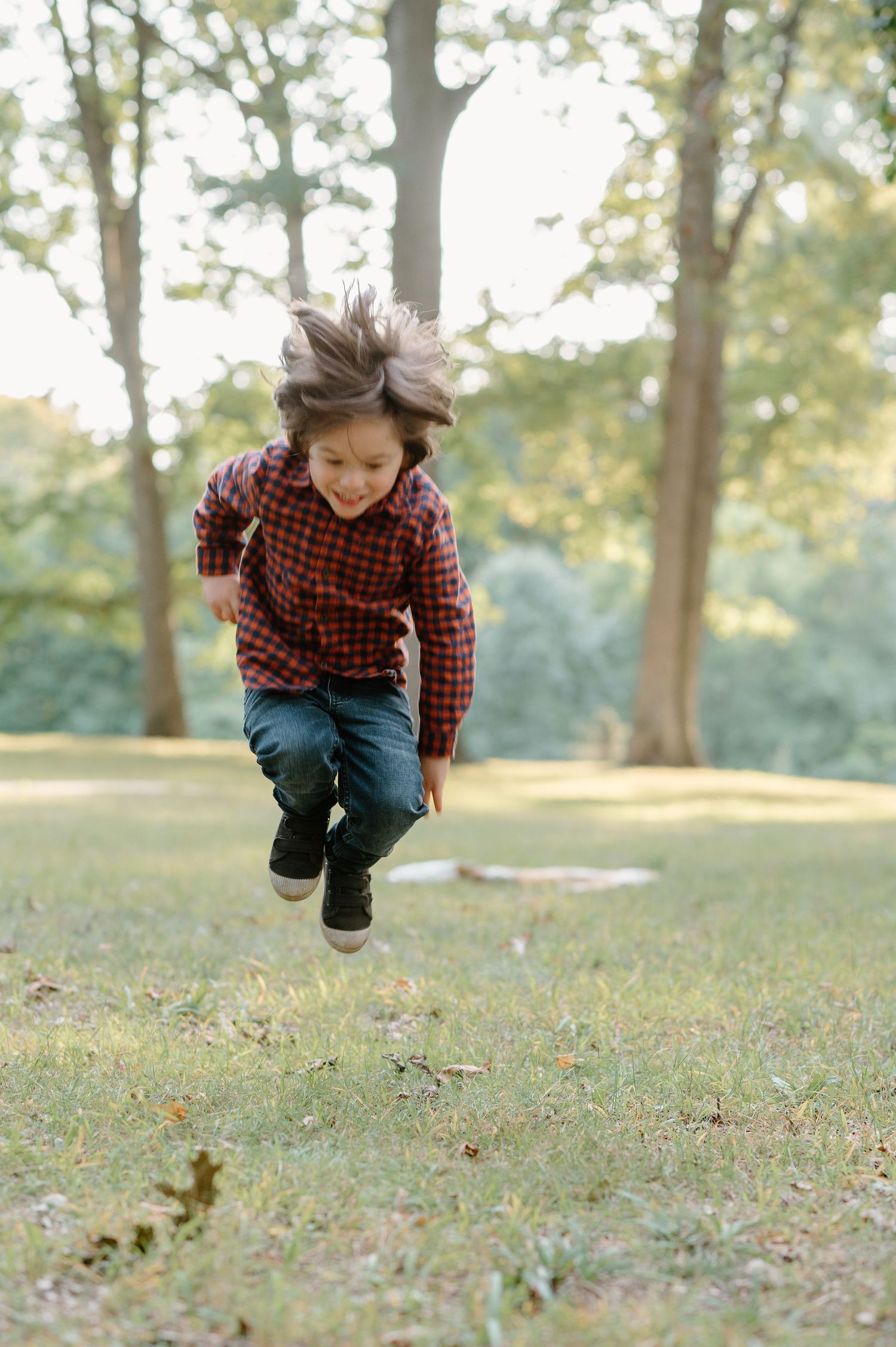 Child in plaid shirt leaping and playing in fallen leaves during autumn.