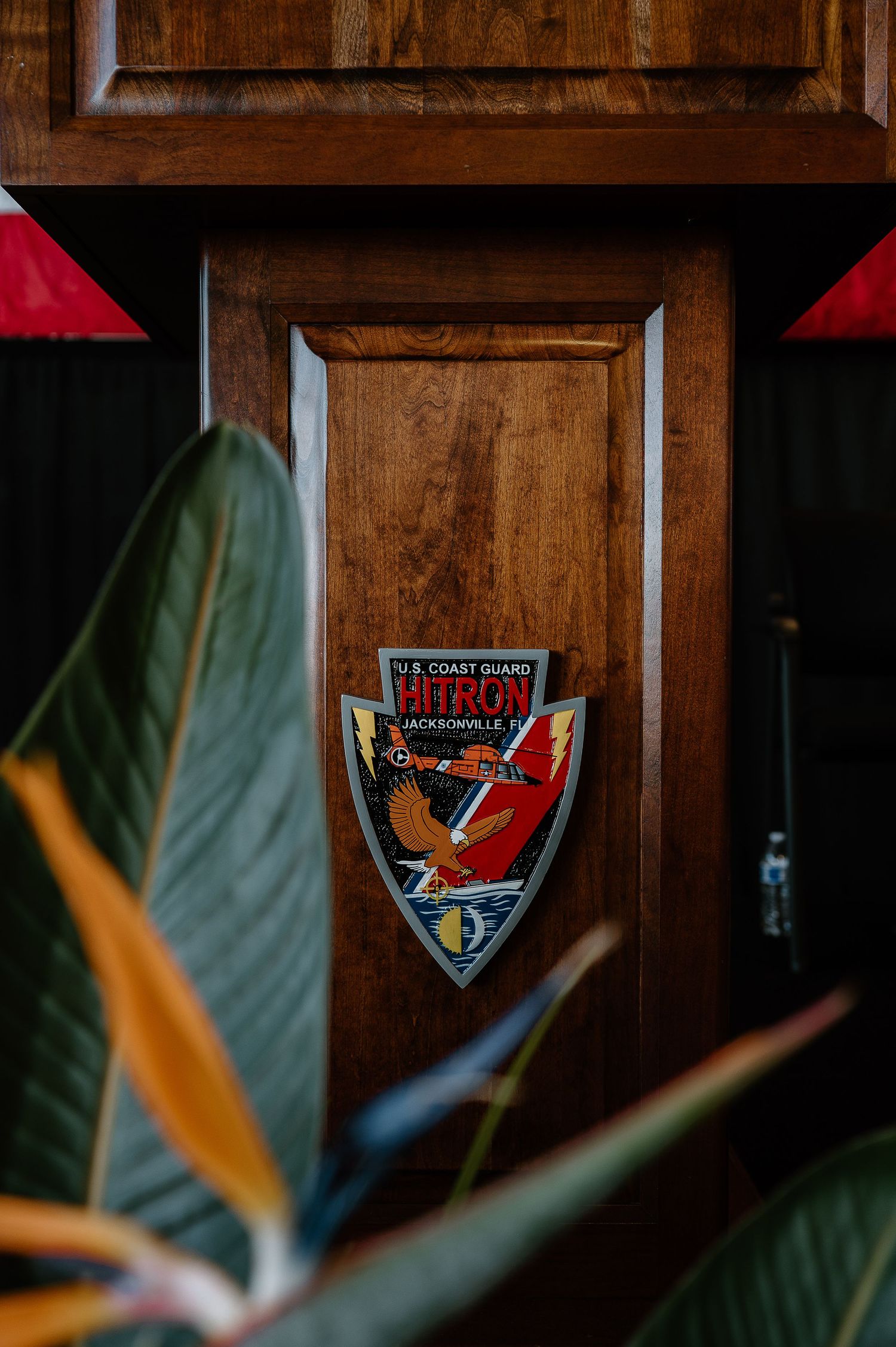 U.S. Coast Guard Patron Jacksonville, FL shield emblem mounted on a rich wooden door with tropical plants in foreground.