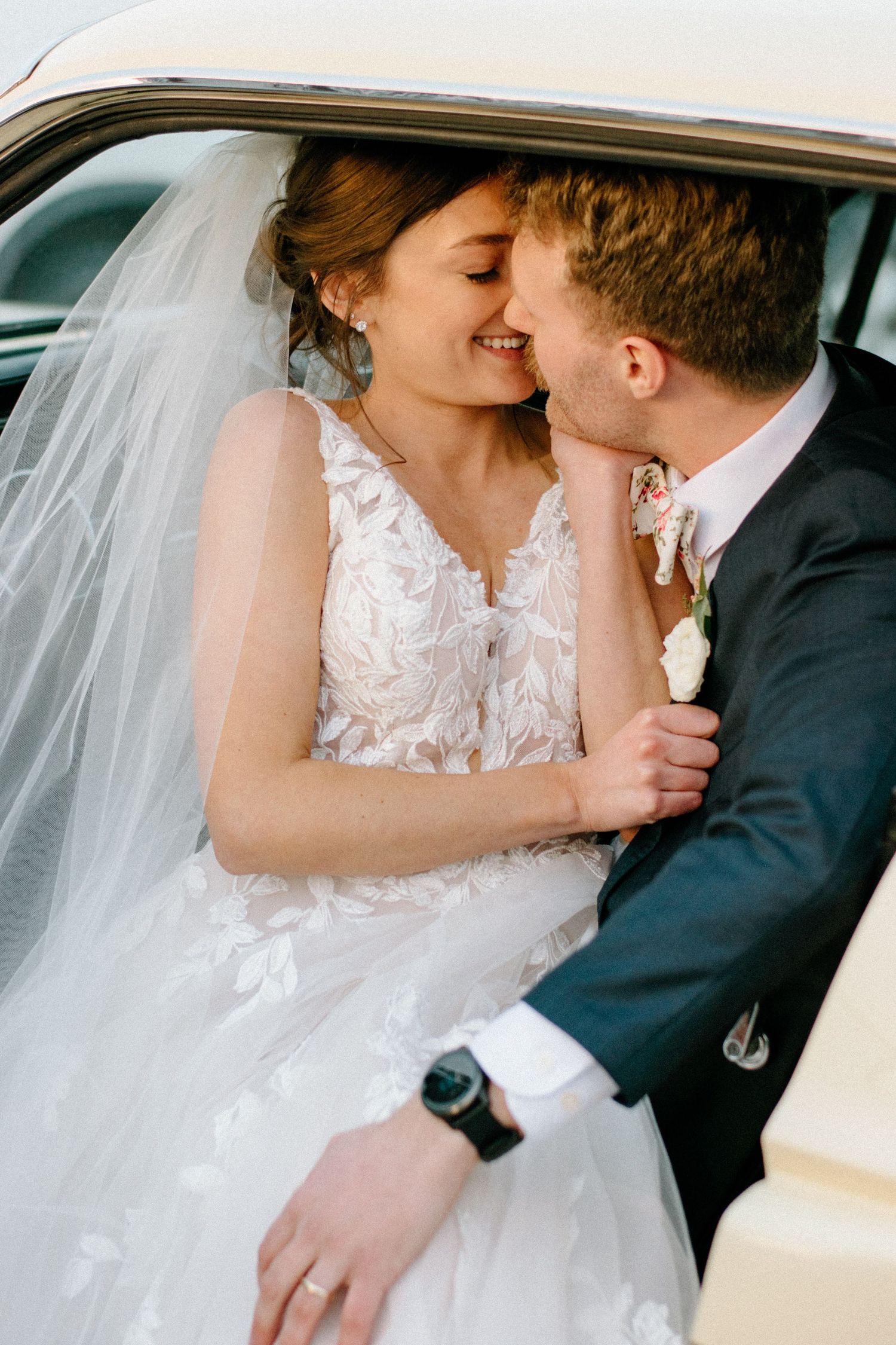 Tender wedding moment captured through a car window with flowing white veil details.