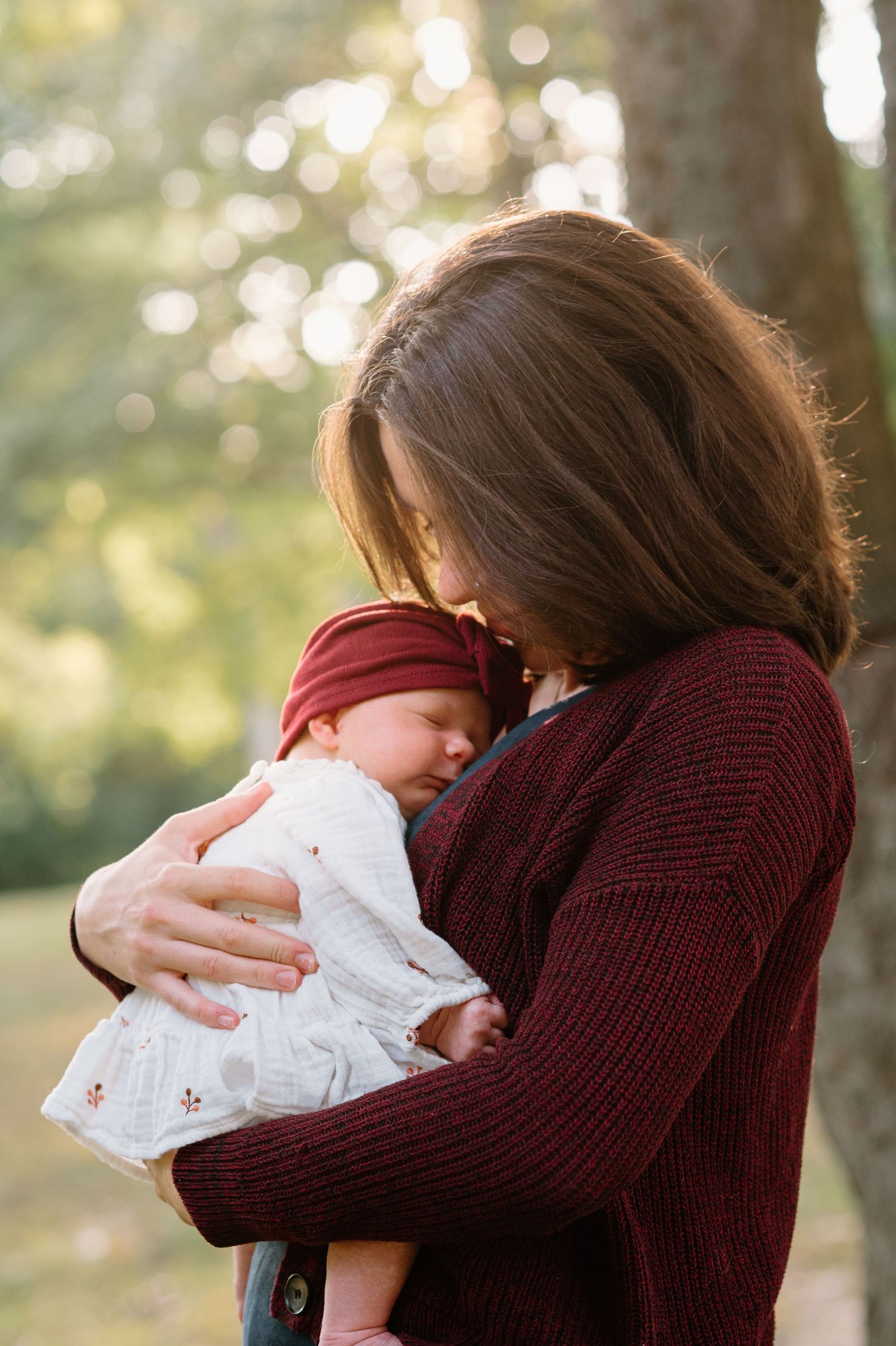 A tender moment showing someone holding a baby in a burgundy sweater against a soft autumn background.