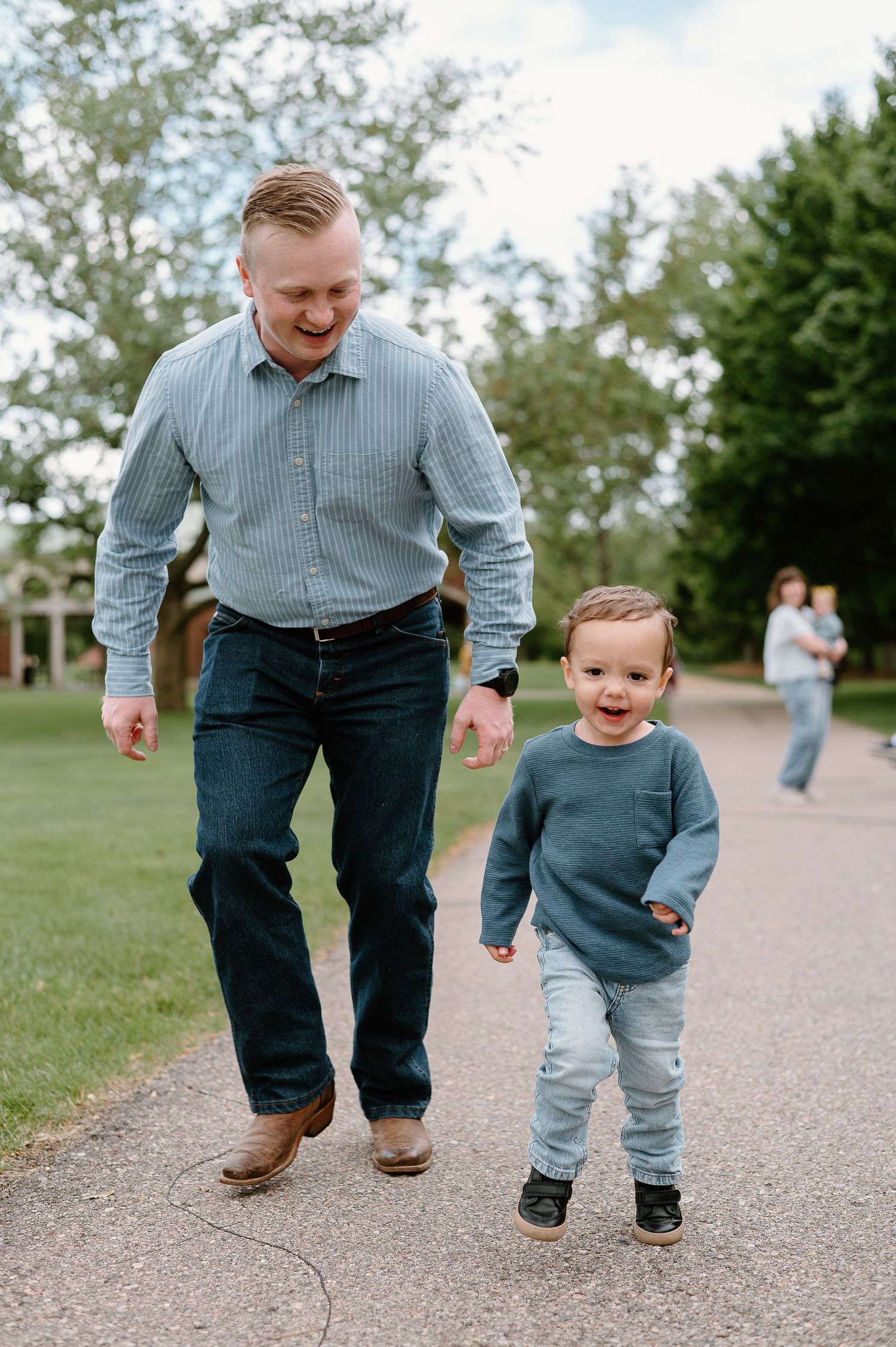 Adult and small child walk together on a path through a green park.