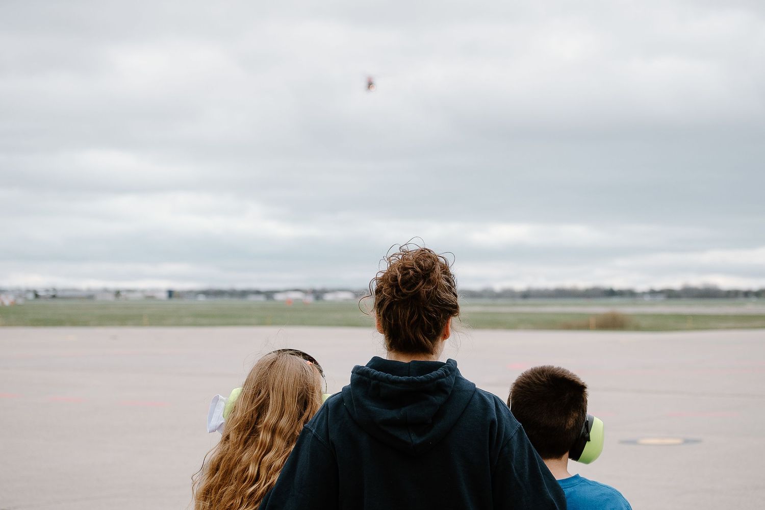 People watching aircraft from the edge of an airfield on an overcast day.