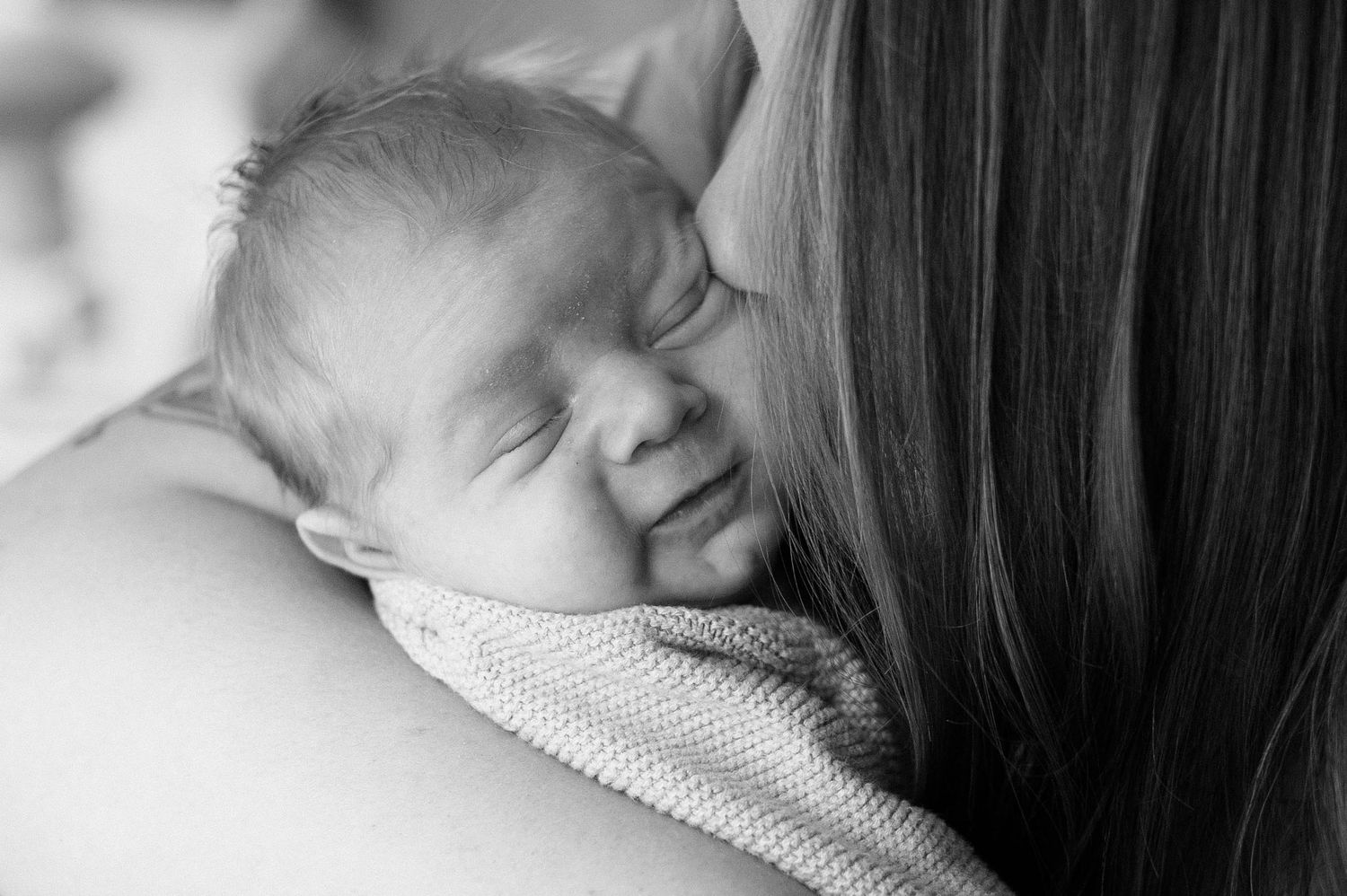 Black and white close-up of sleeping newborn resting on shoulder.