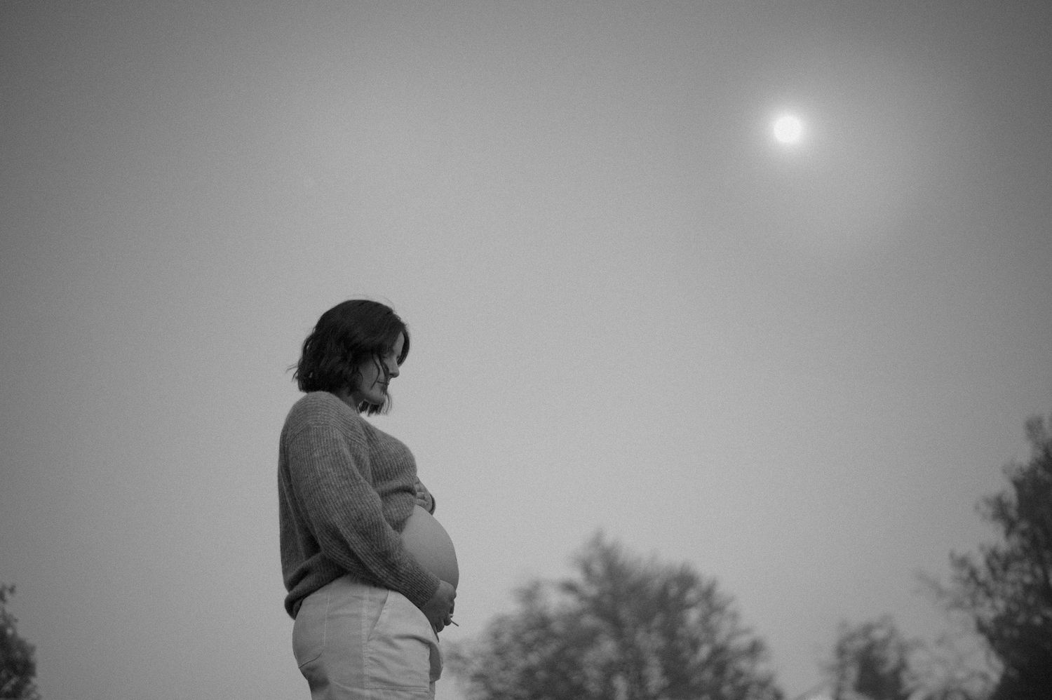 Silhouetted figure against misty gray sky with sun peeking through clouds.