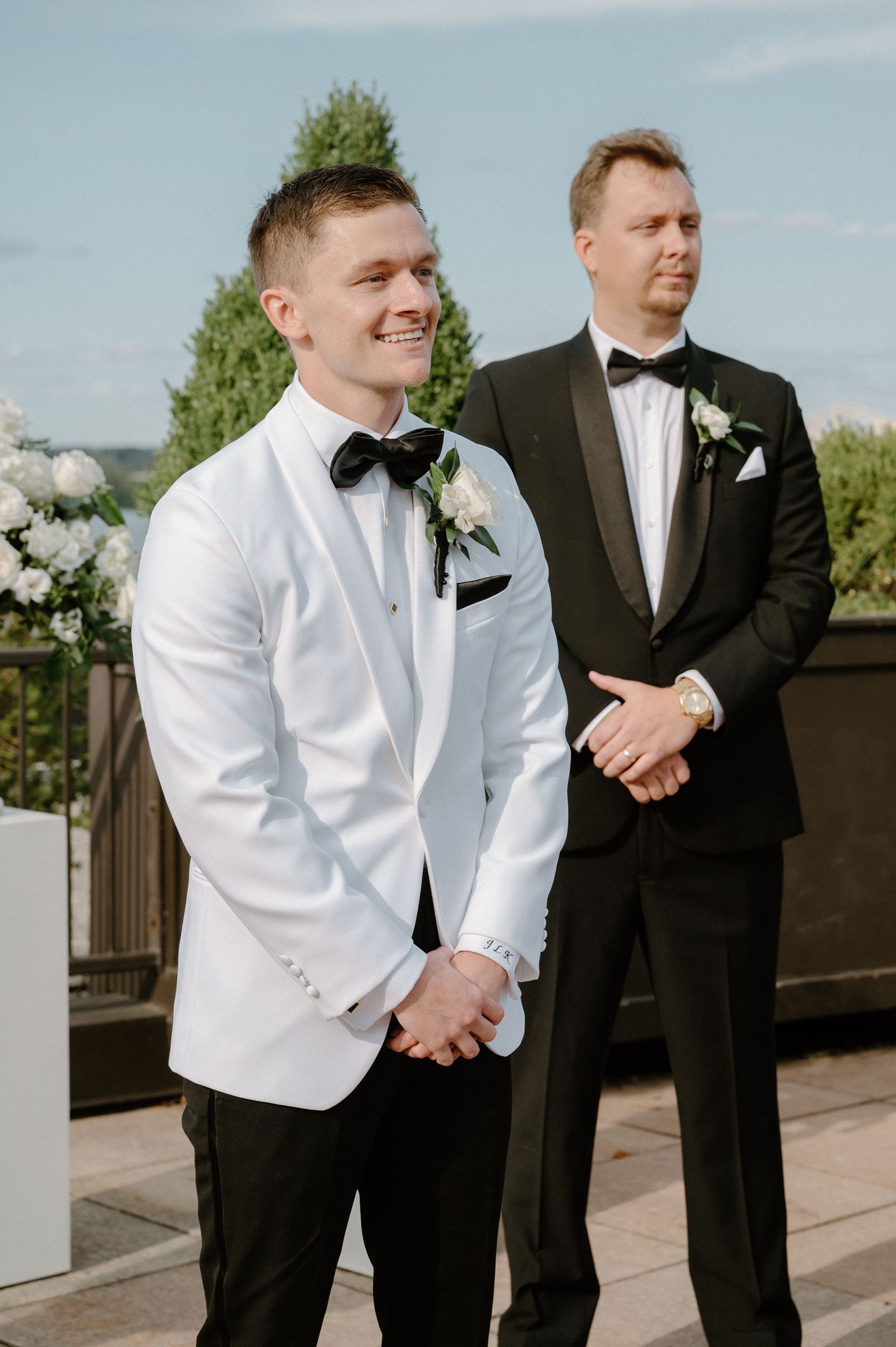 Wedding party members in formal attire standing on outdoor terrace.