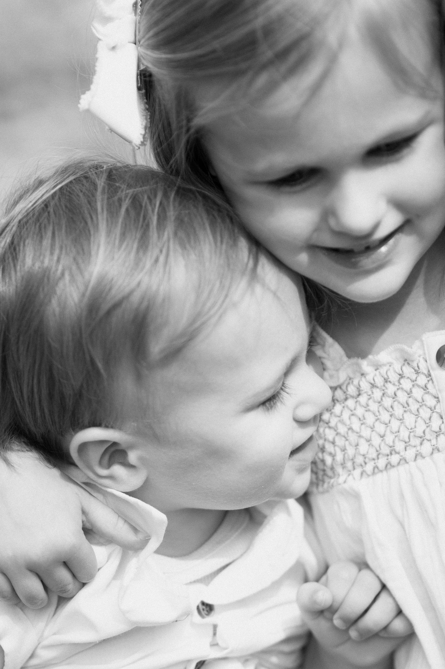 Two children share a sweet candid moment together in black and white photography.