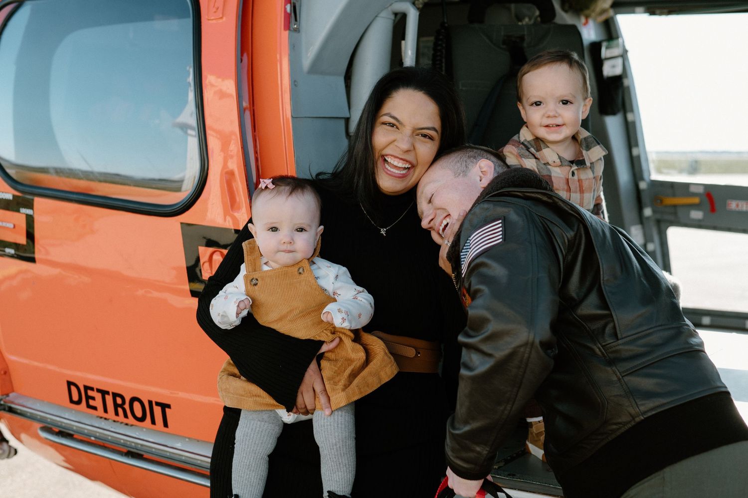 Family posing together in and around orange vintage Detroit vehicle during photo session.