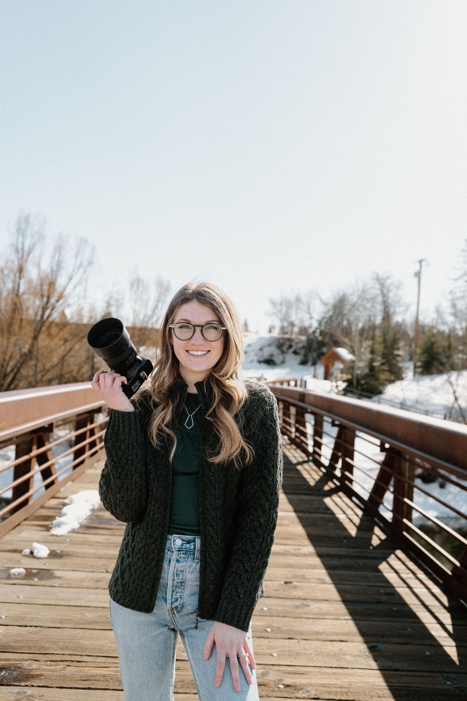 Lifestyle portraits captured on a wooden bridge walkway against a snowy winter landscape.
