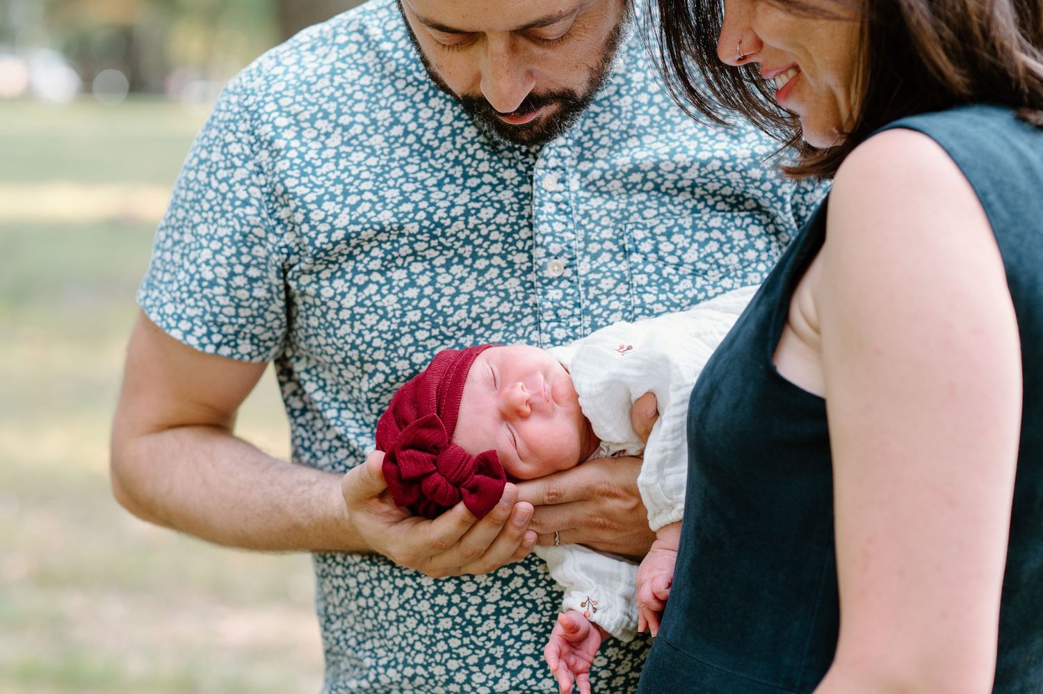 A couple gazes lovingly at their newborn baby wearing a red hat.