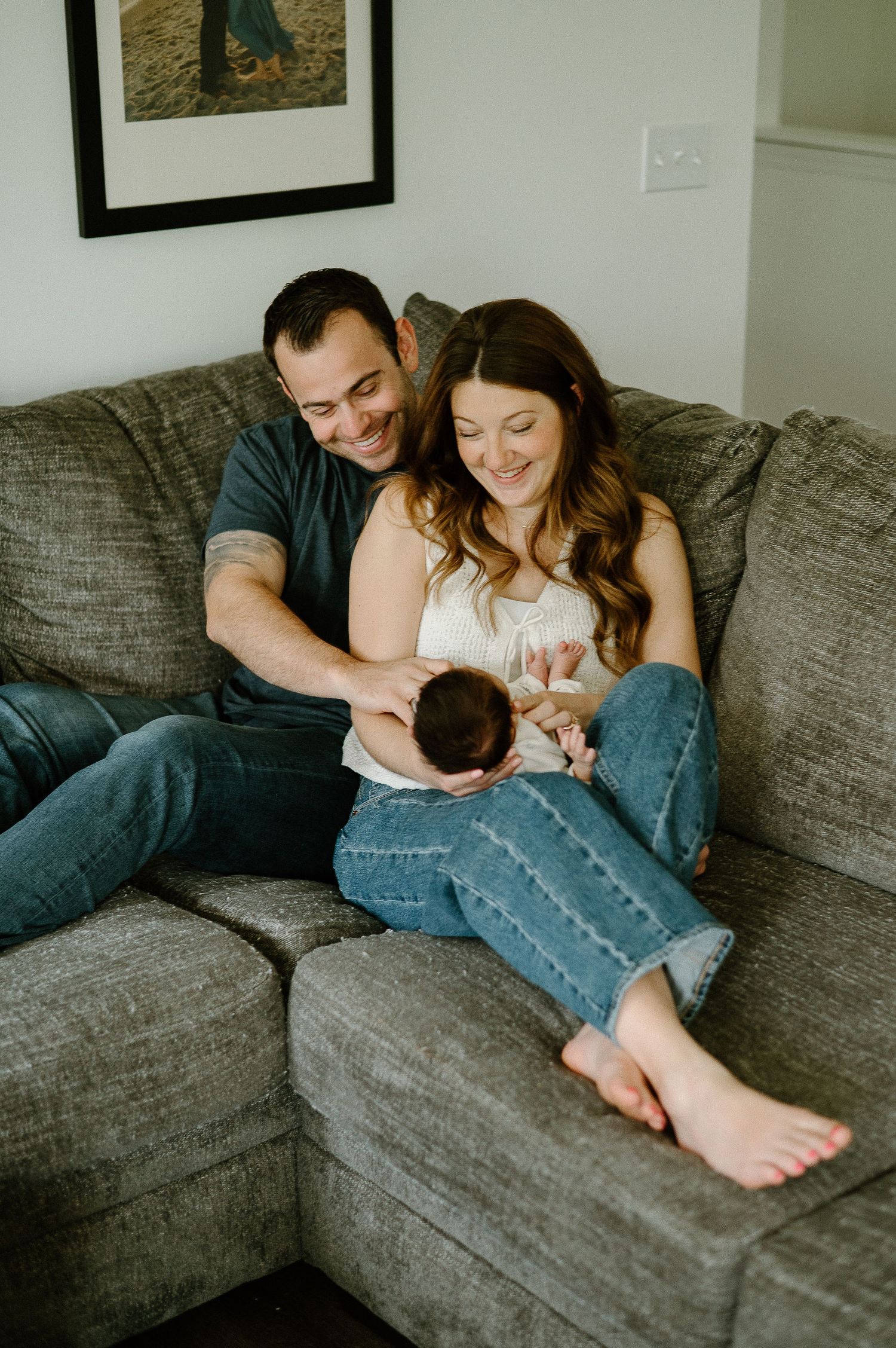 A cozy family moment on a grey couch in a living room with framed art on the wall.