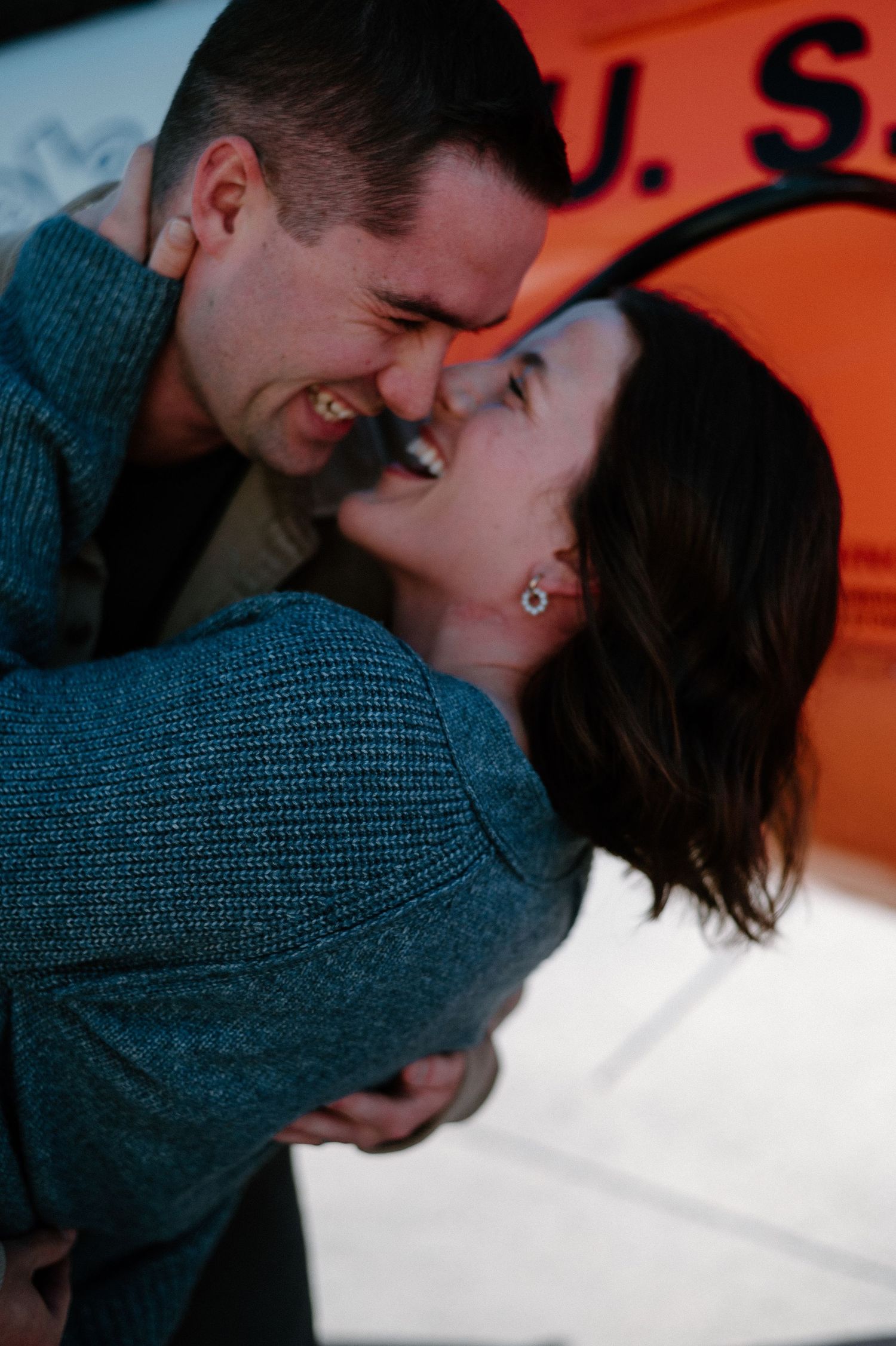 Romantic couple share intimate moment against orange sunset backdrop.