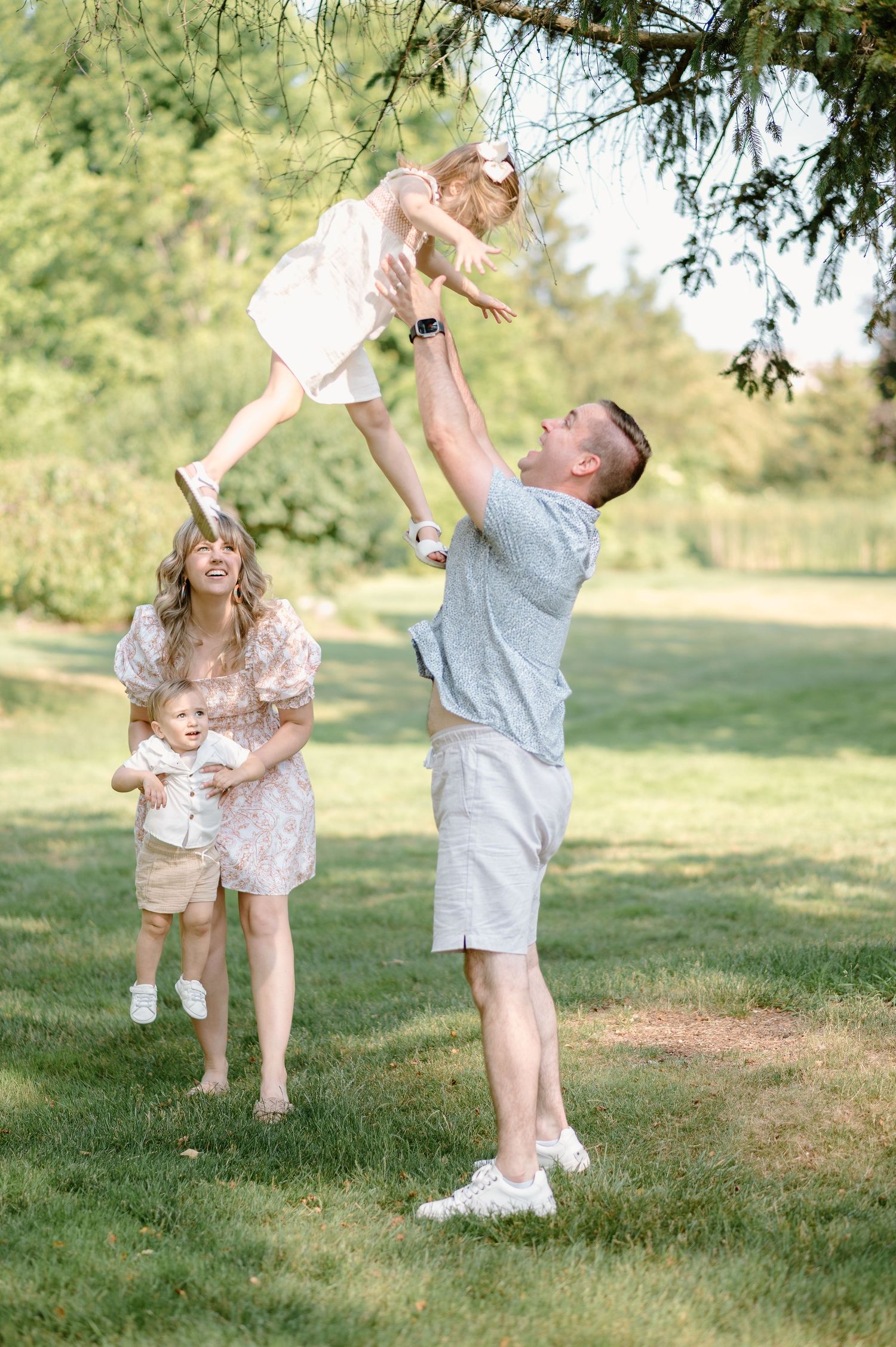 A joyful family moment in a sunny park as parents play and lift their child in the air.