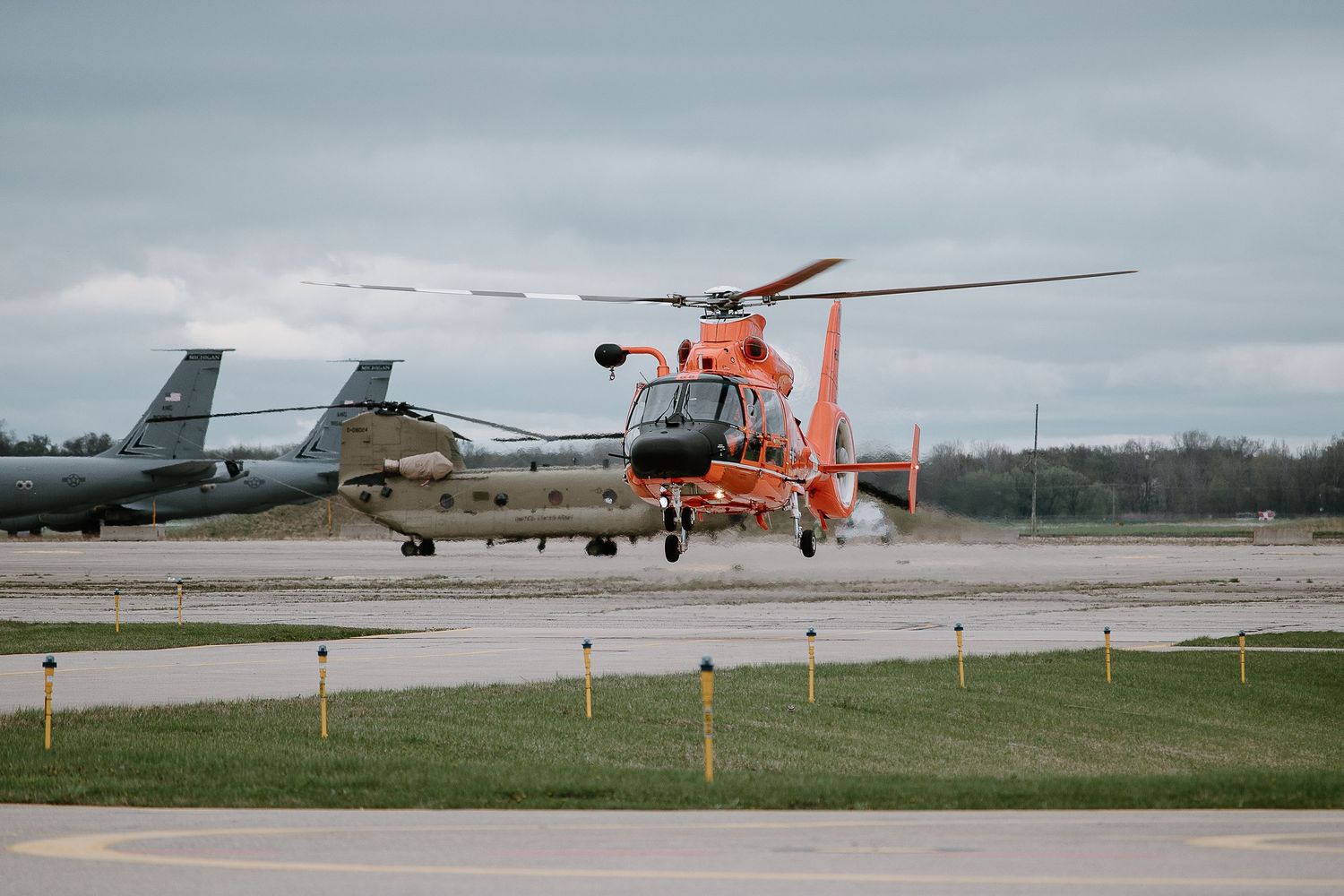 Coast Guard helicopters and aircraft parked on a military airfield tarmac.