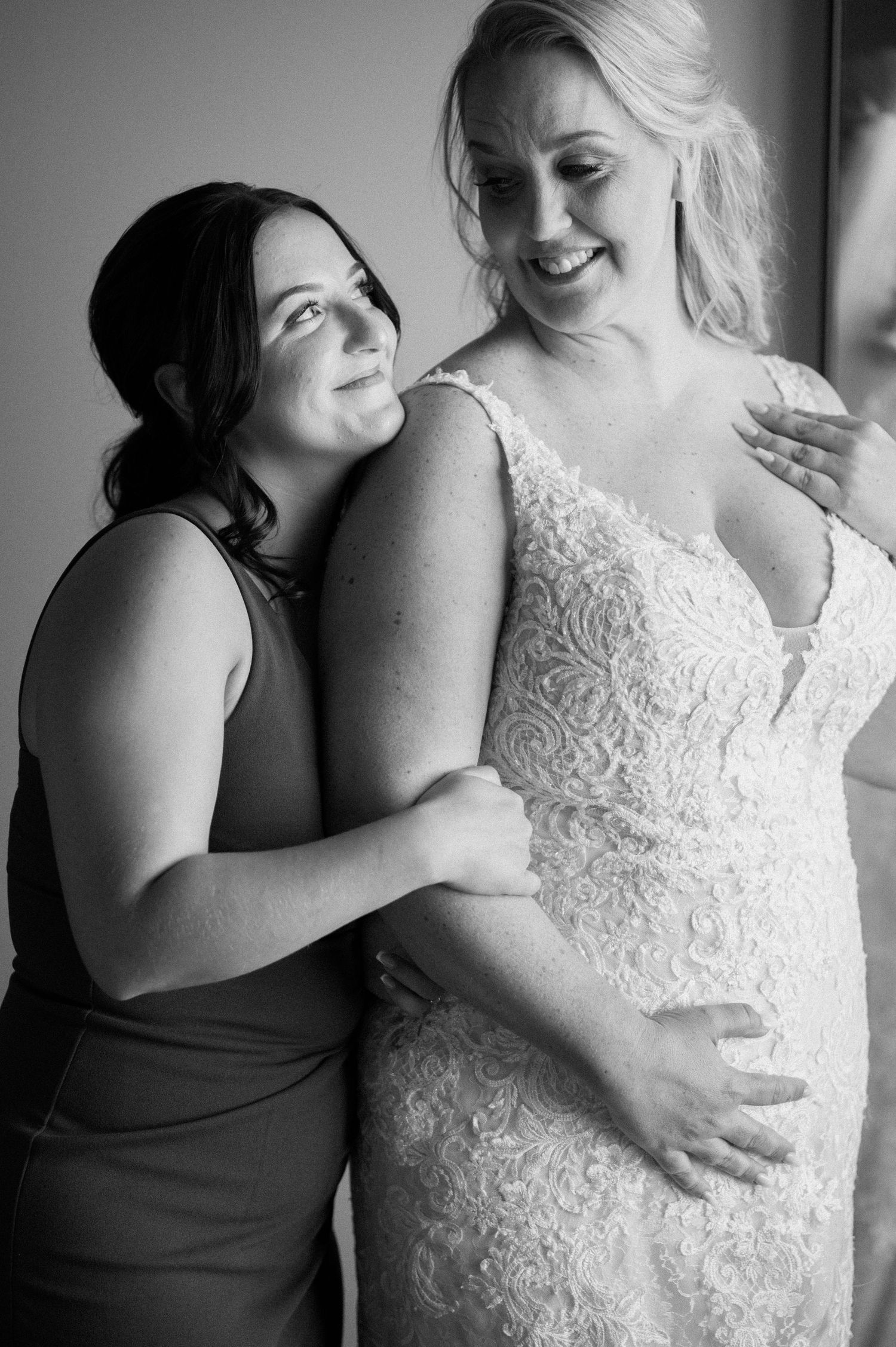 Black and white emotional moment between bridesmaid and bride in lace gown.
