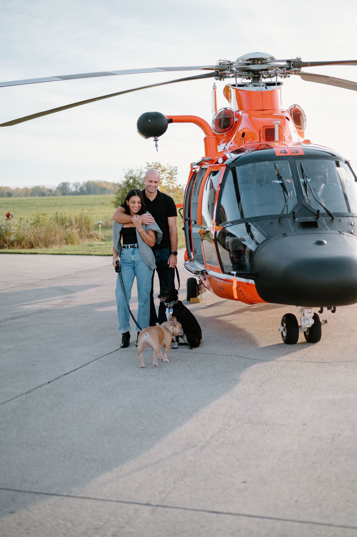 Coast Guard helicopter crew stands on tarmac next to bright orange rescue aircraft.