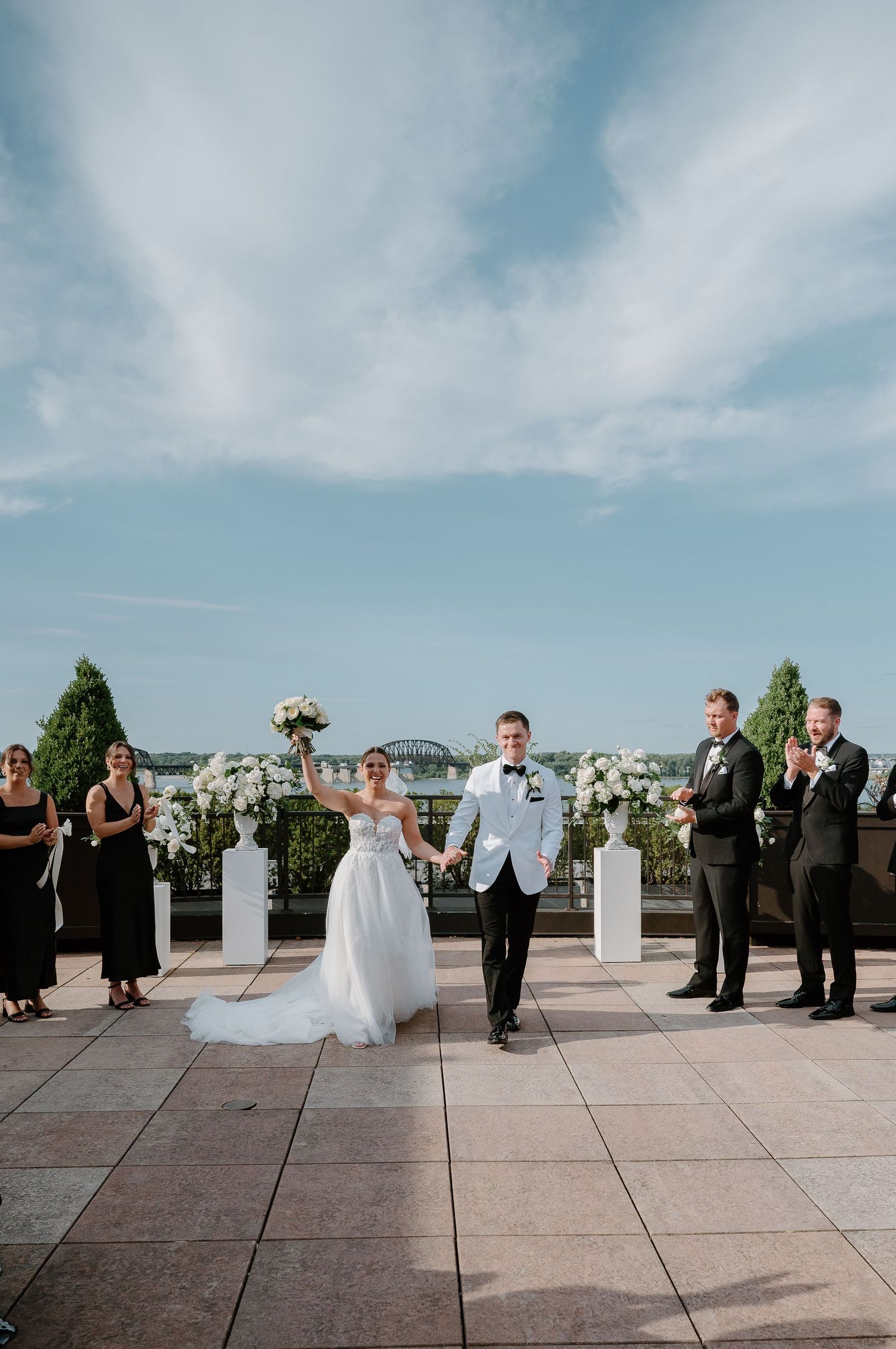 Wedding party gathered on outdoor terrace with city views in background.