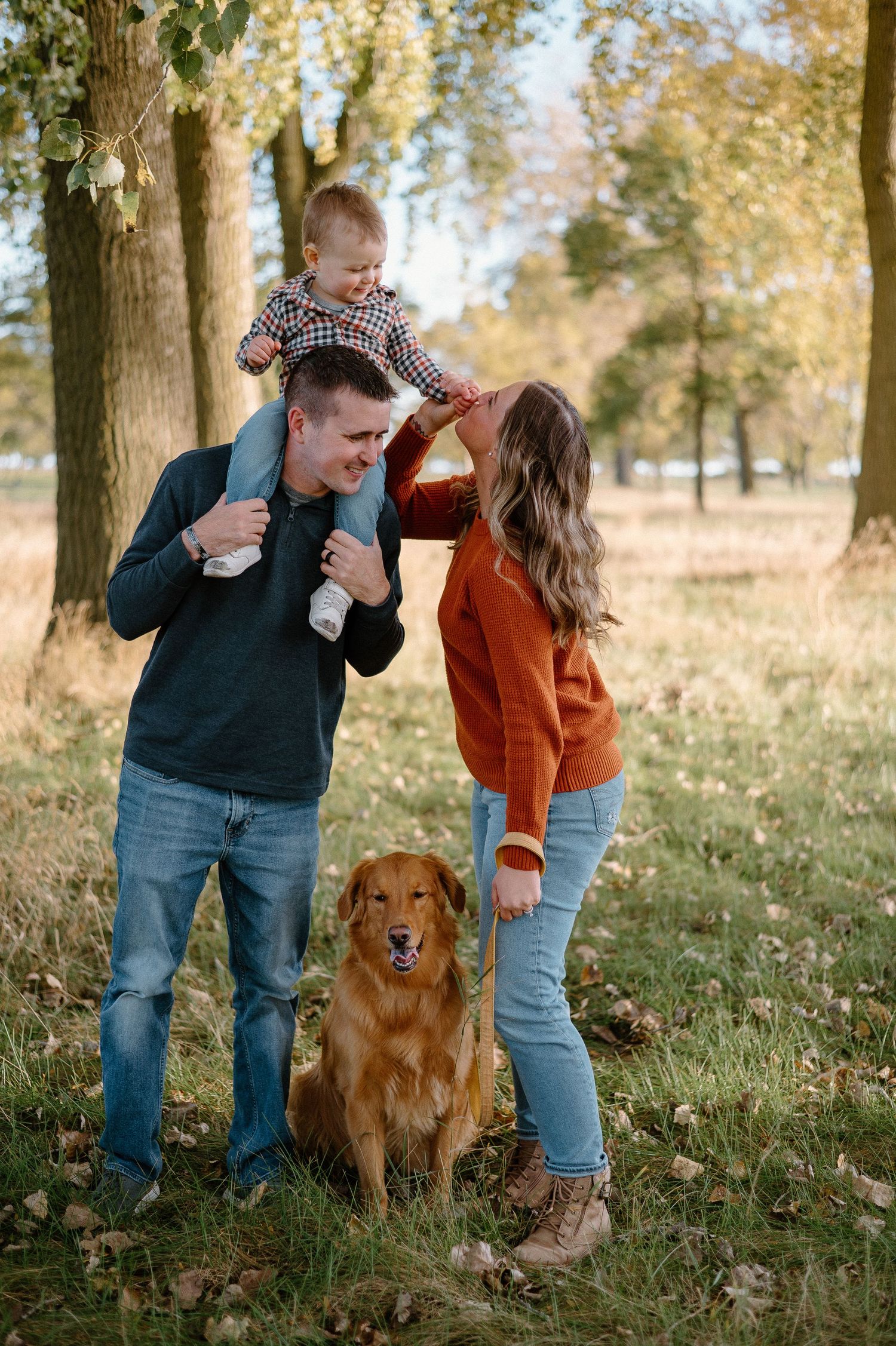 Playful couple dancing with their golden retriever in a wooded setting.