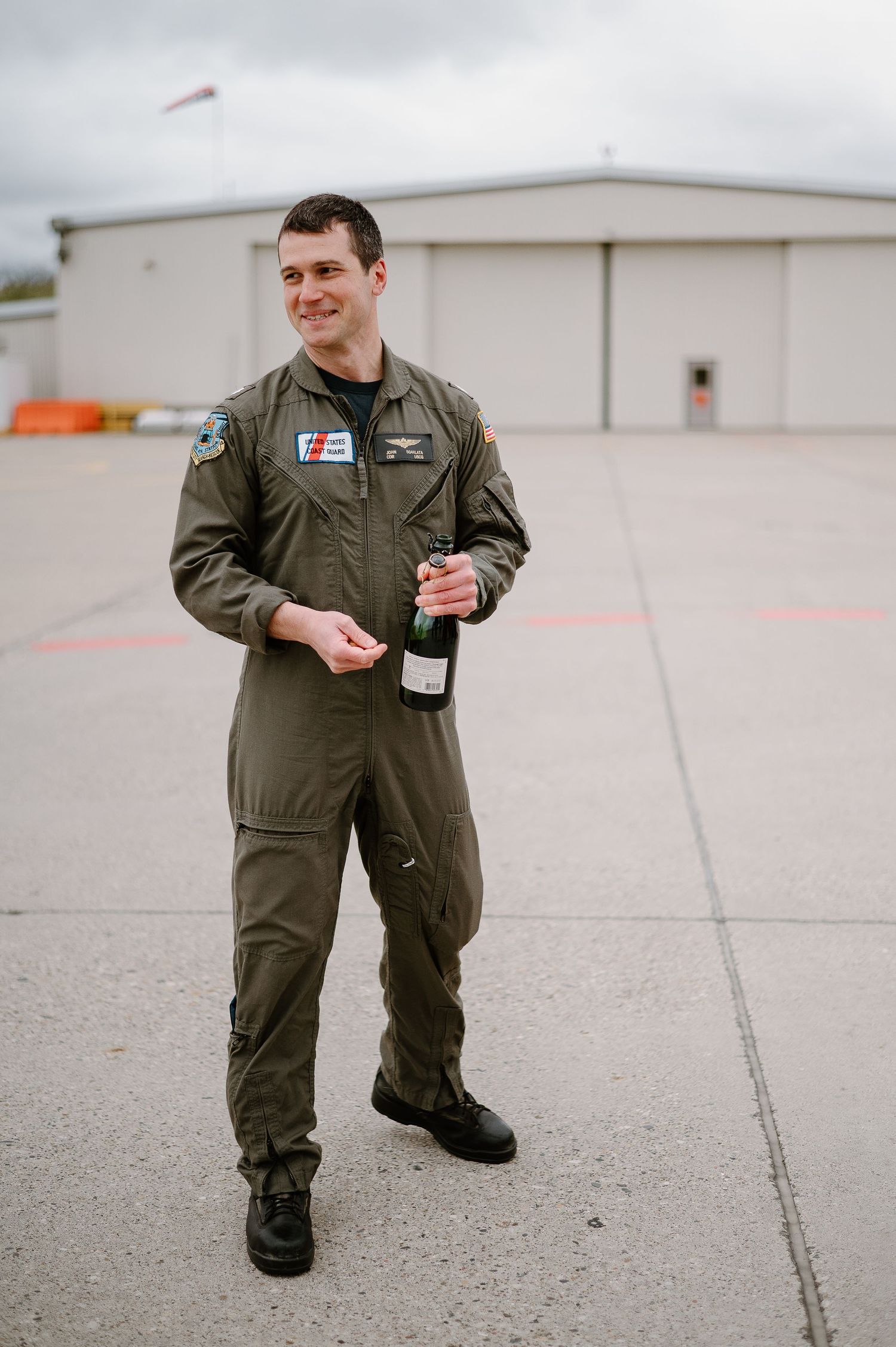 Coast Guard pilot in olive flight suit standing on airfield tarmac.