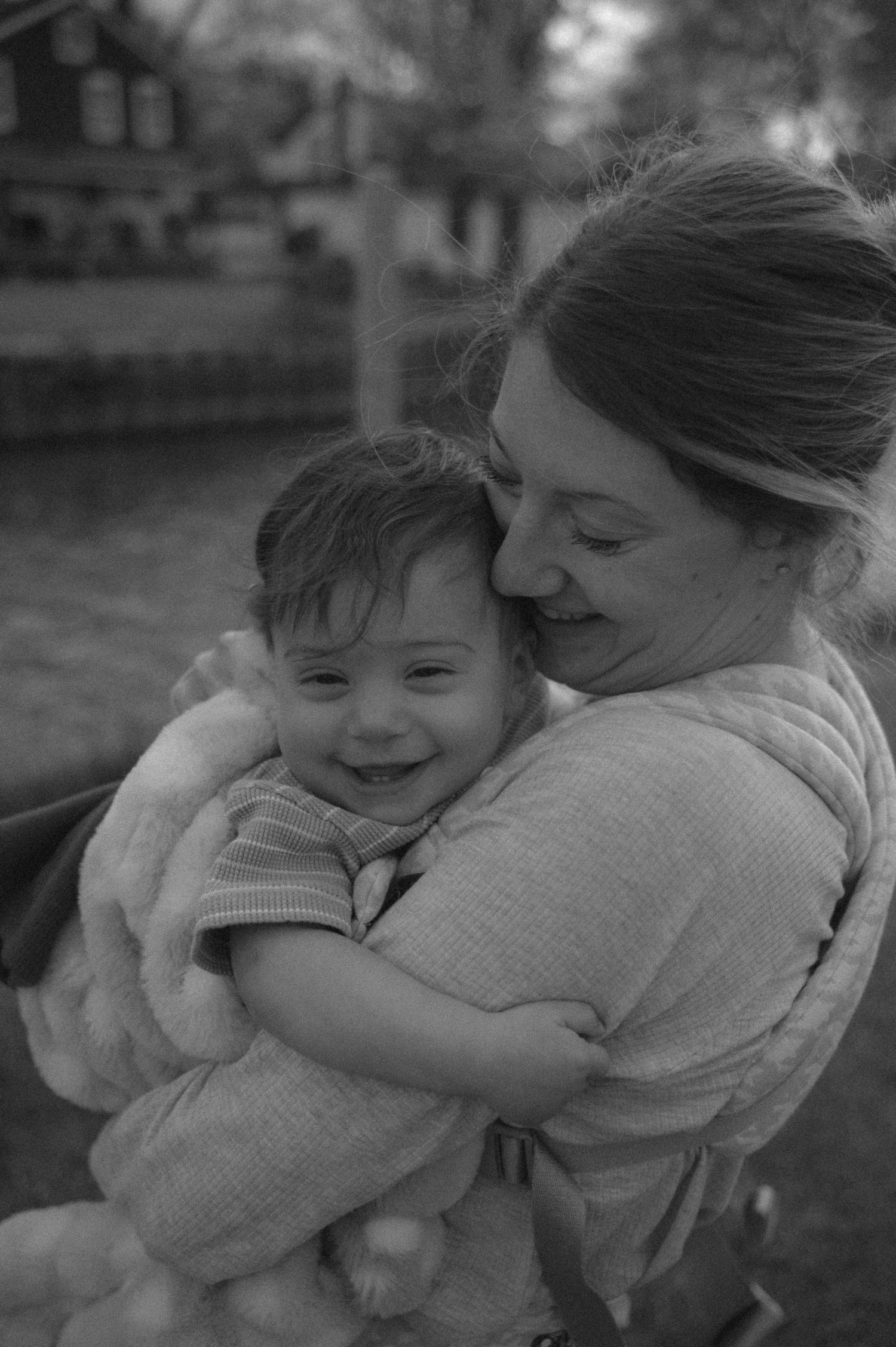 Black and white photo of a smiling baby being lovingly cradled by a woman outdoors.
