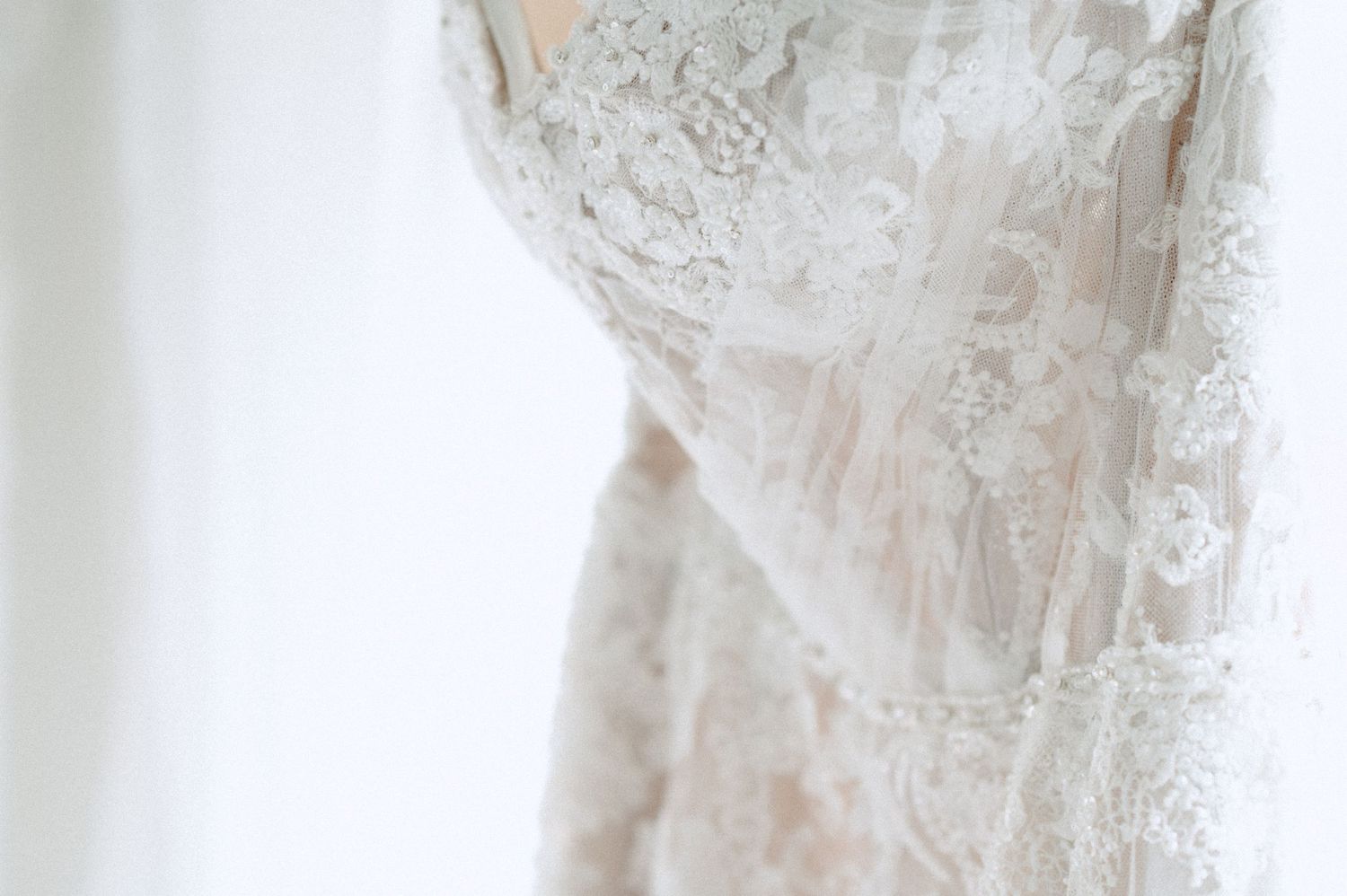 Close-up details of delicate white lace wedding dress fabric and beading.