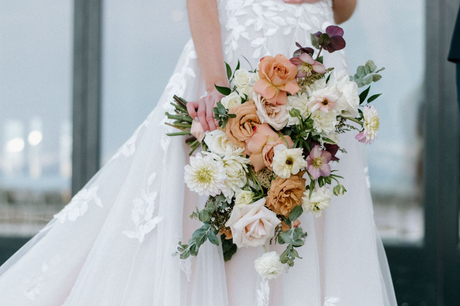 Elegant bridal bouquet with white and peach roses, delicate greenery and soft accents against a light background.