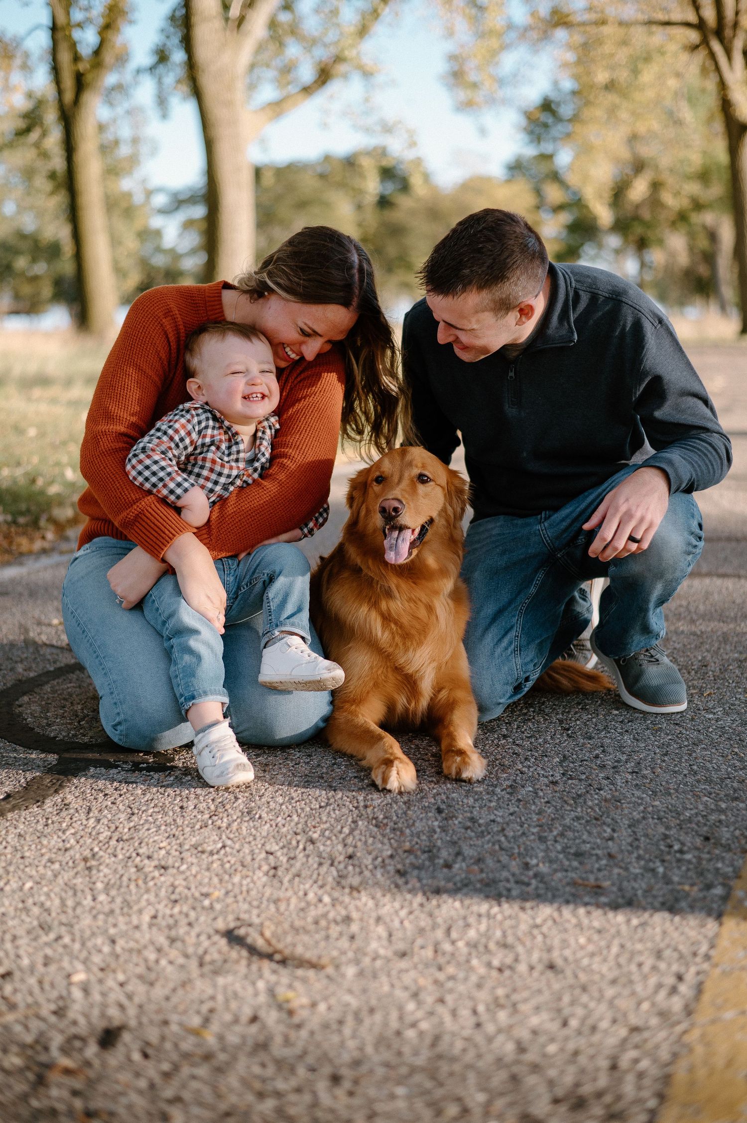 Family and golden retriever dog sitting together on gravel path during sunset.