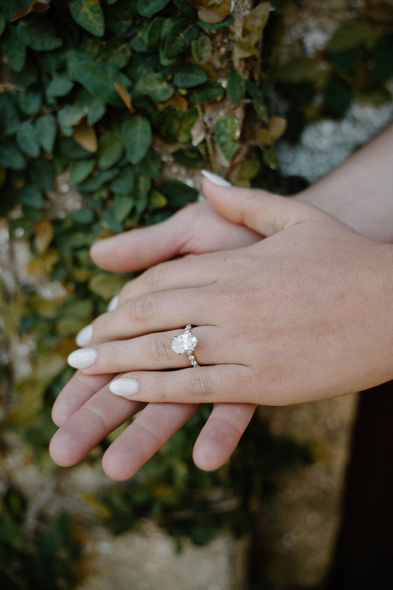 Close-up of a woman's hands displaying a stunning oval diamond solitaire engagement ring on her ring finger.