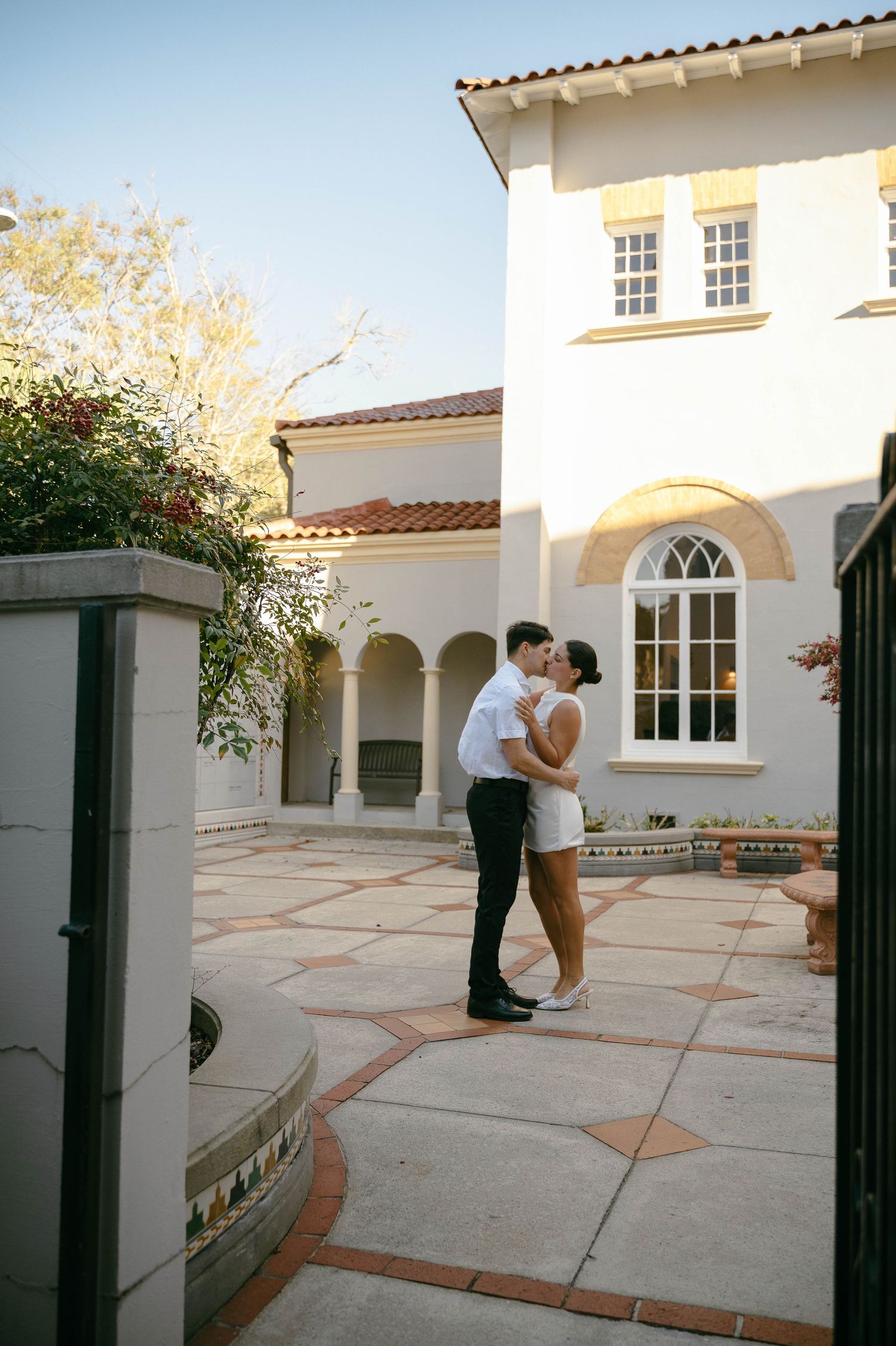 Couple sharing a romantic kiss in a courtyard of an elegant Mediterranean-style white villa.