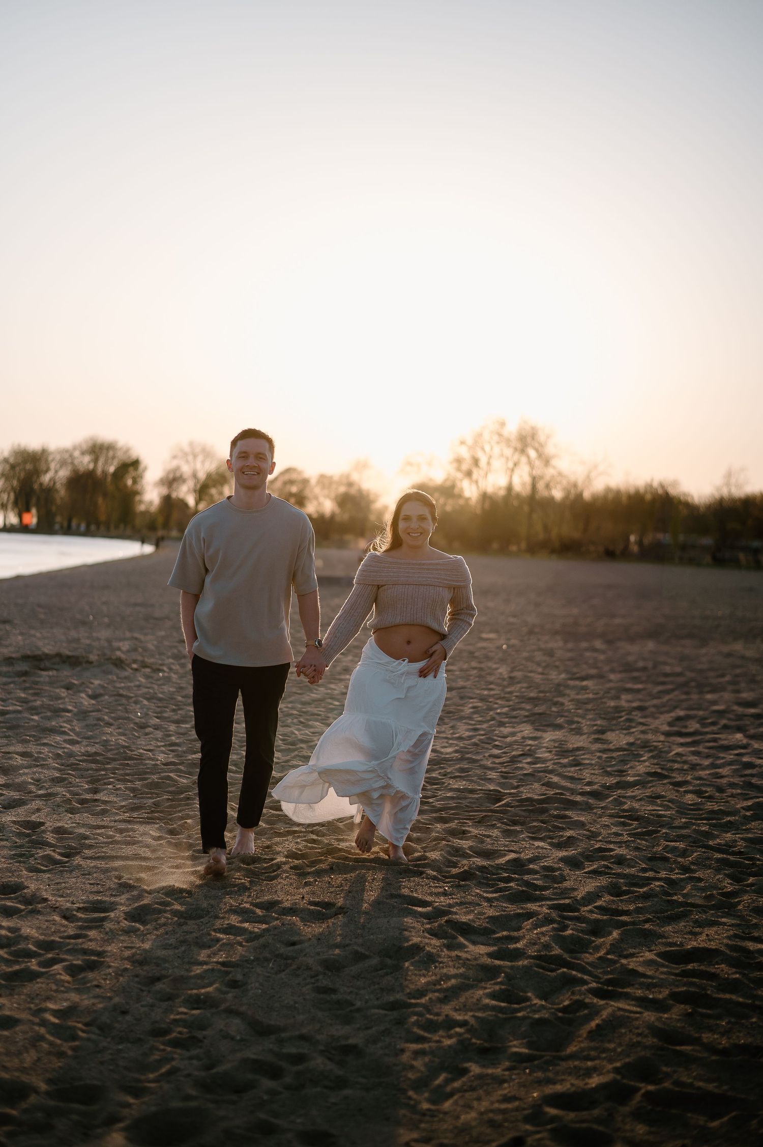 A couple walks on a beach during sunset holding their baby.