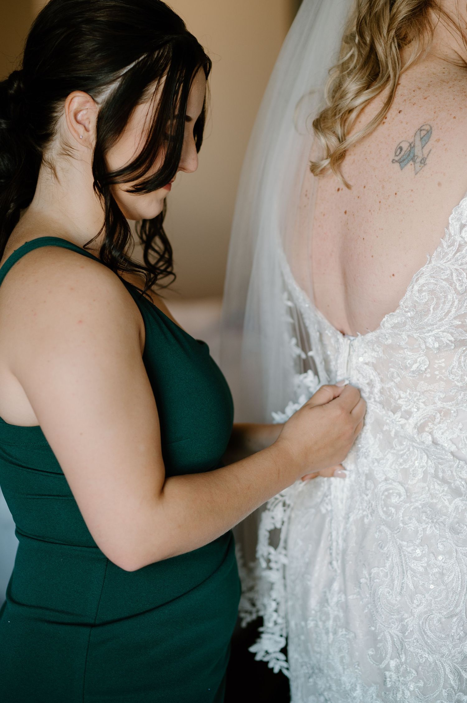 Bridesmaid in dark green dress helping with white lace wedding gown details.