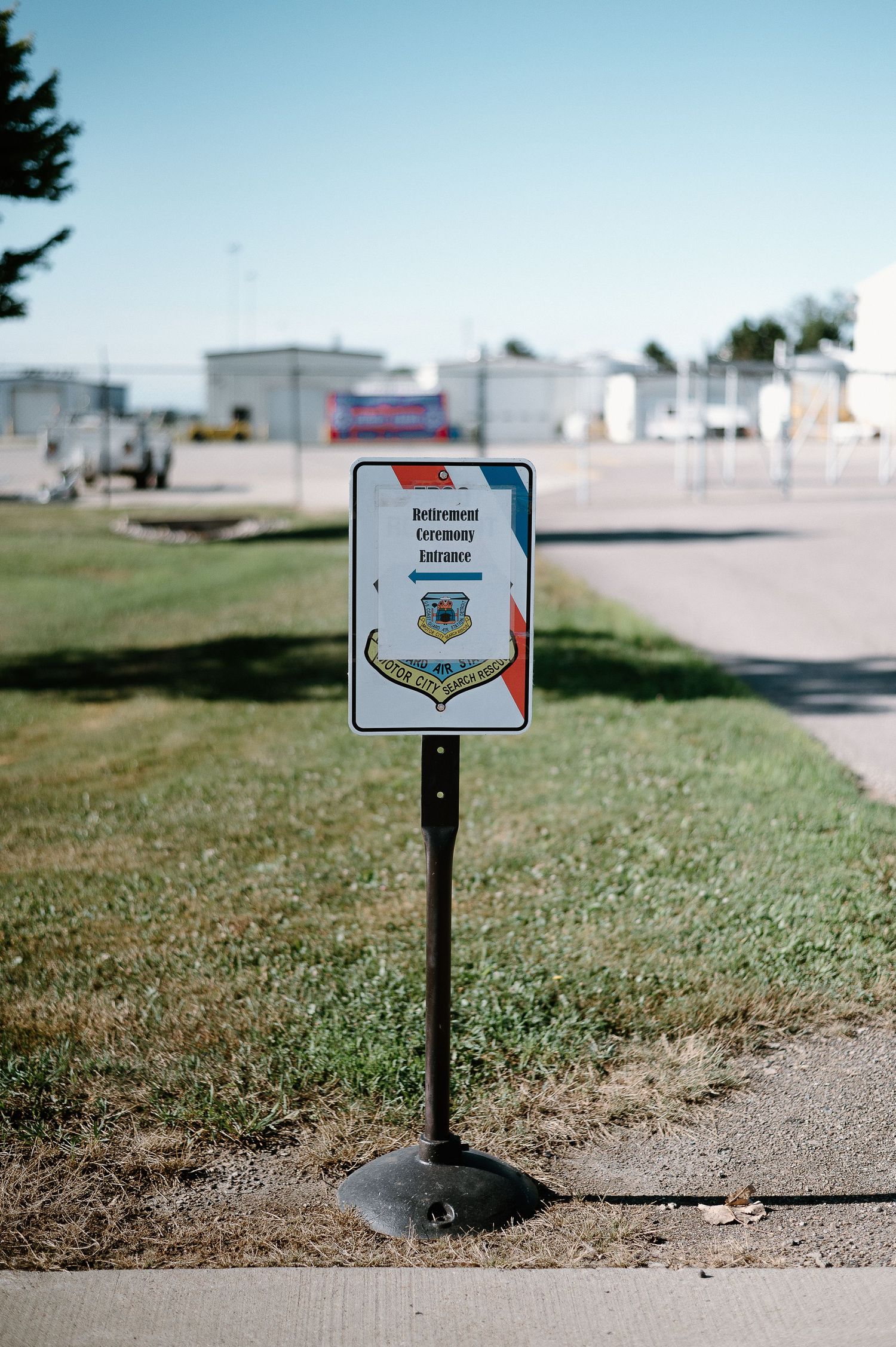 Directional signs stand on posts along a grassy path near a military facility.