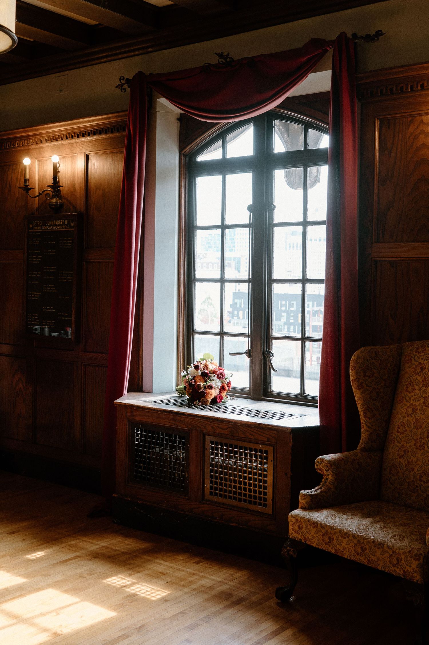 Elegant window alcove with burgundy drapes, wooden paneling, and a floral arrangement in warm sunlight.