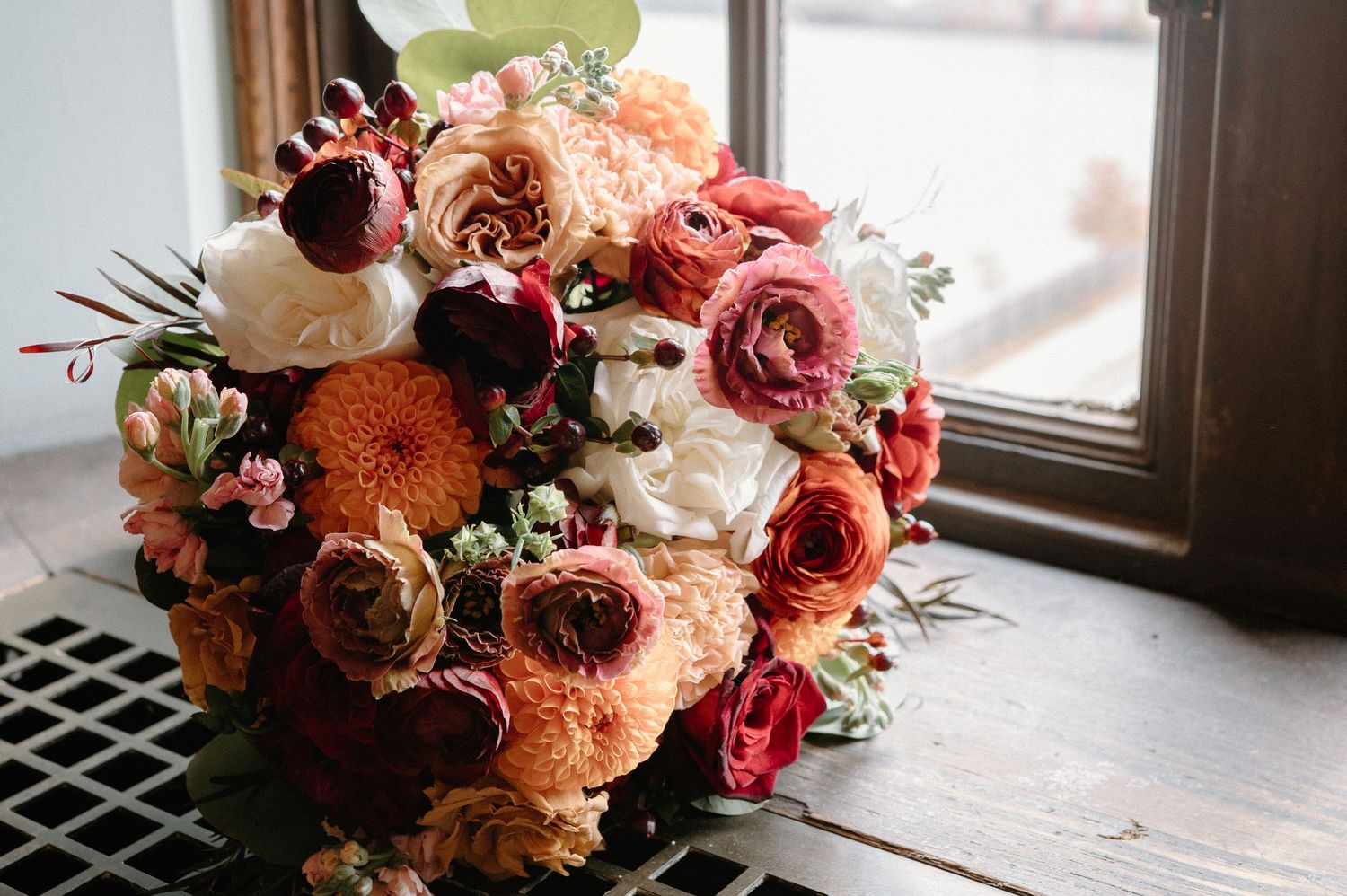 A romantic floral arrangement with pink and peach roses sits elegantly by a window in natural light.