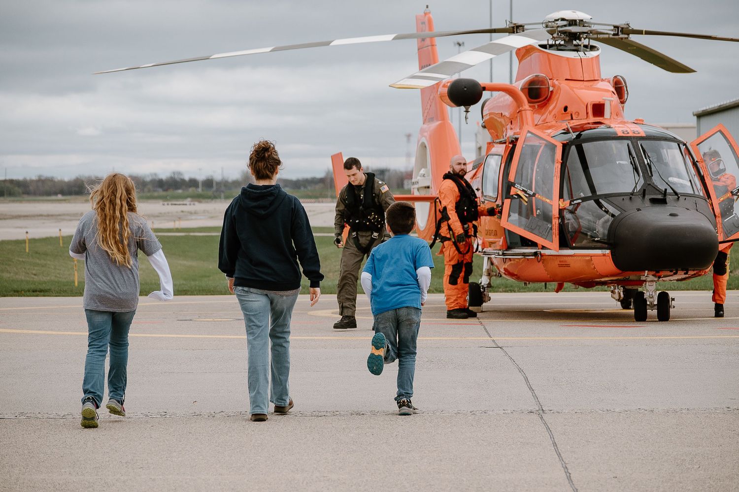 Family walking towards bright orange rescue helicopter on an airfield.