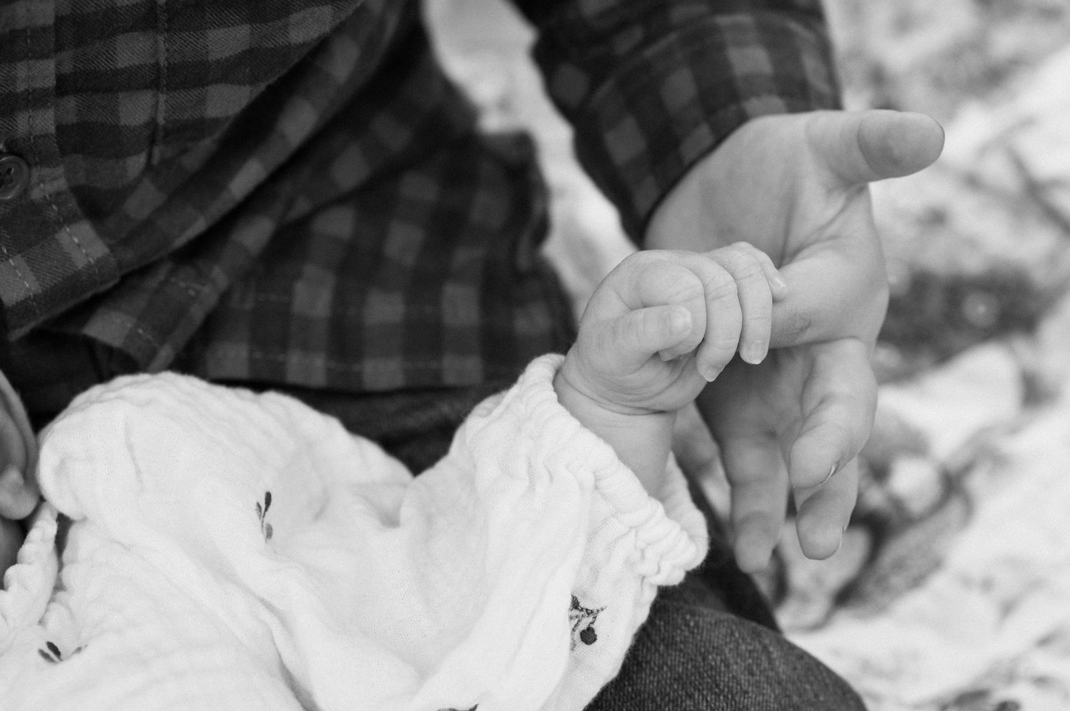 A close-up black and white shot of tiny fingers grasping an adult hand.