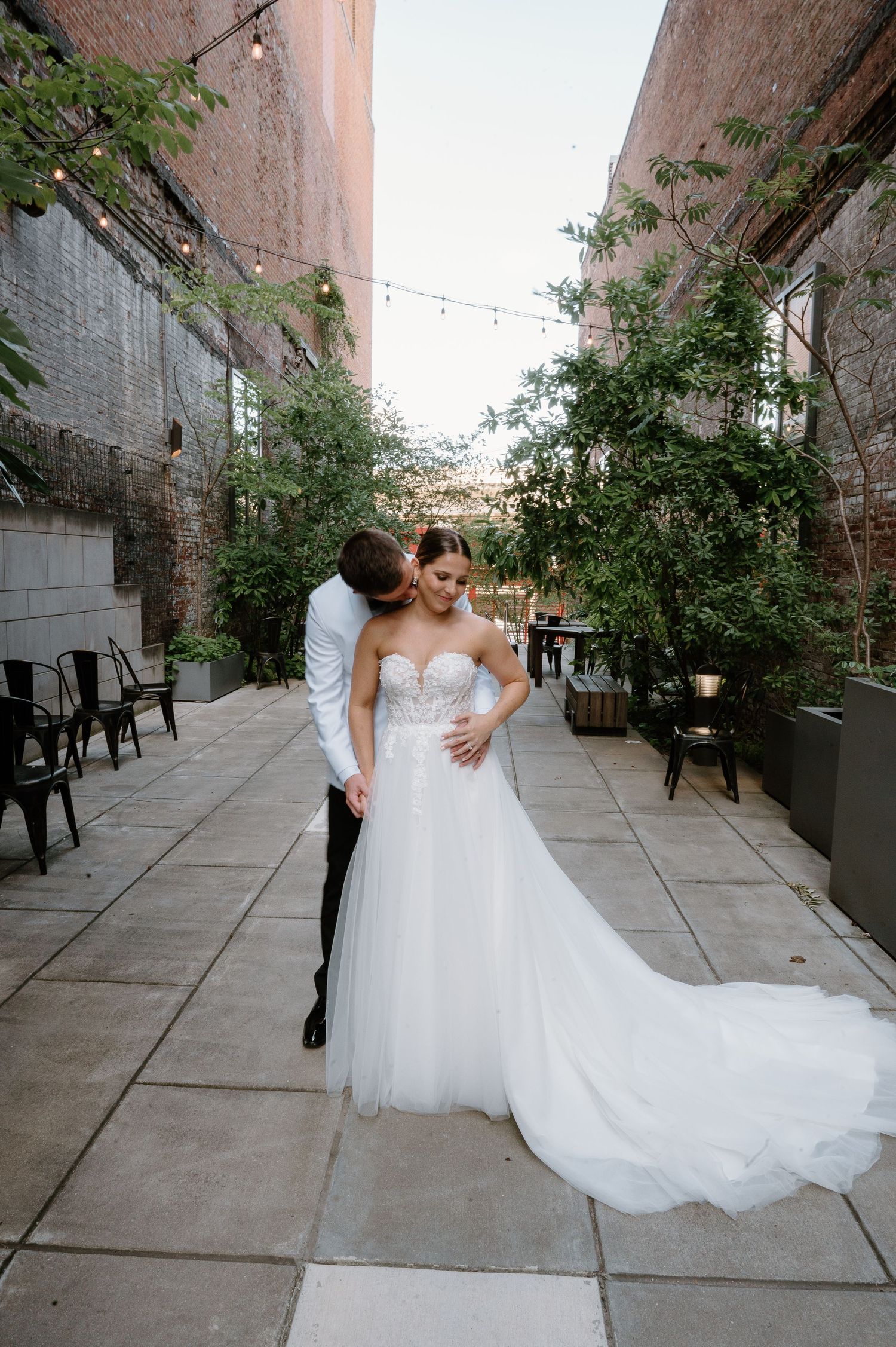 Newlyweds dancing together in an urban courtyard with trailing white wedding dress.