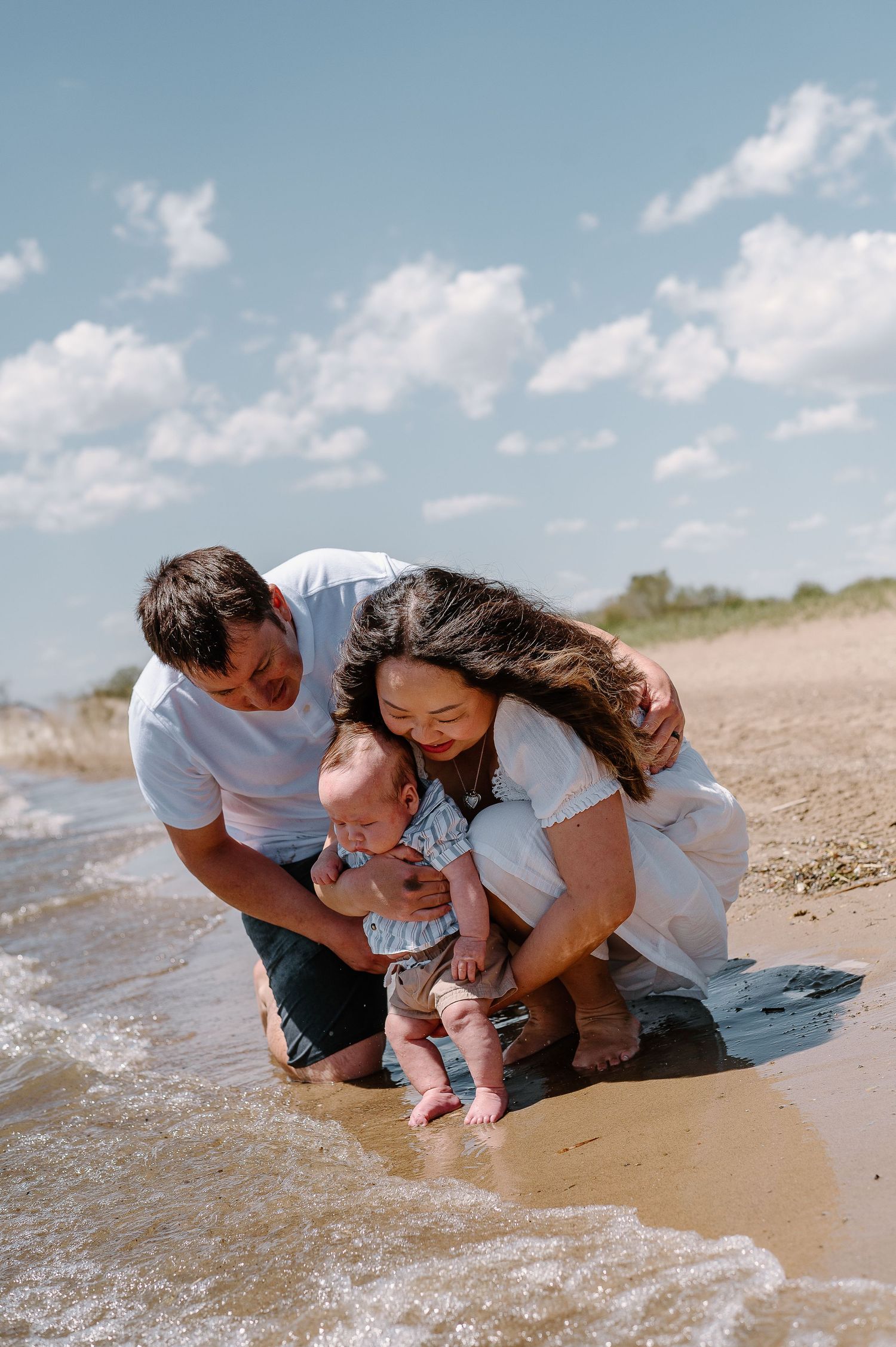 Family playing and laughing together at water's edge on sandy beach.