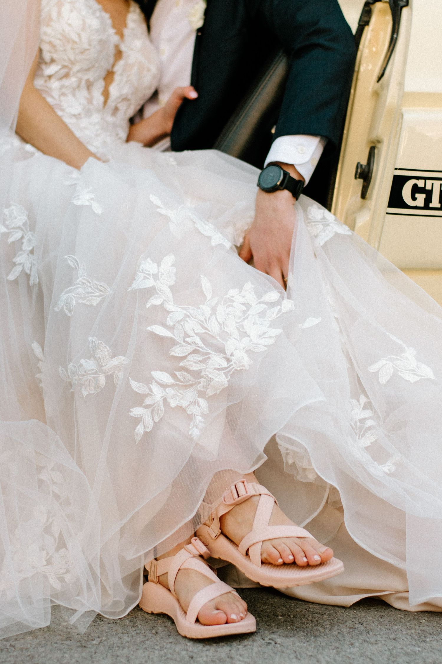Close-up of bridal gown details and nude sandals on light colored flooring.