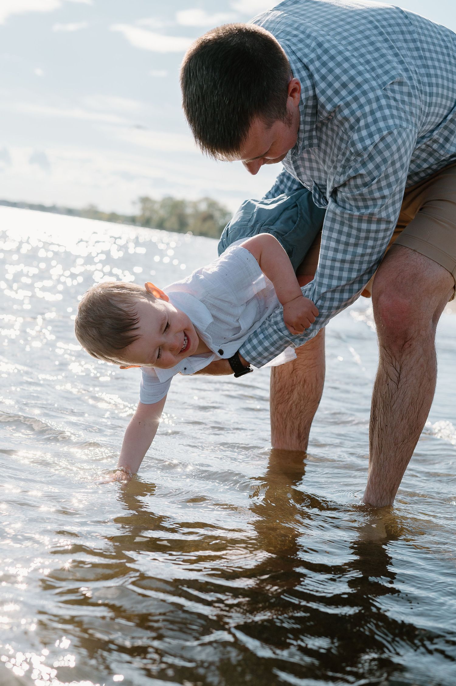 Parent and child exploring the shallow beach water together in golden sunlight.