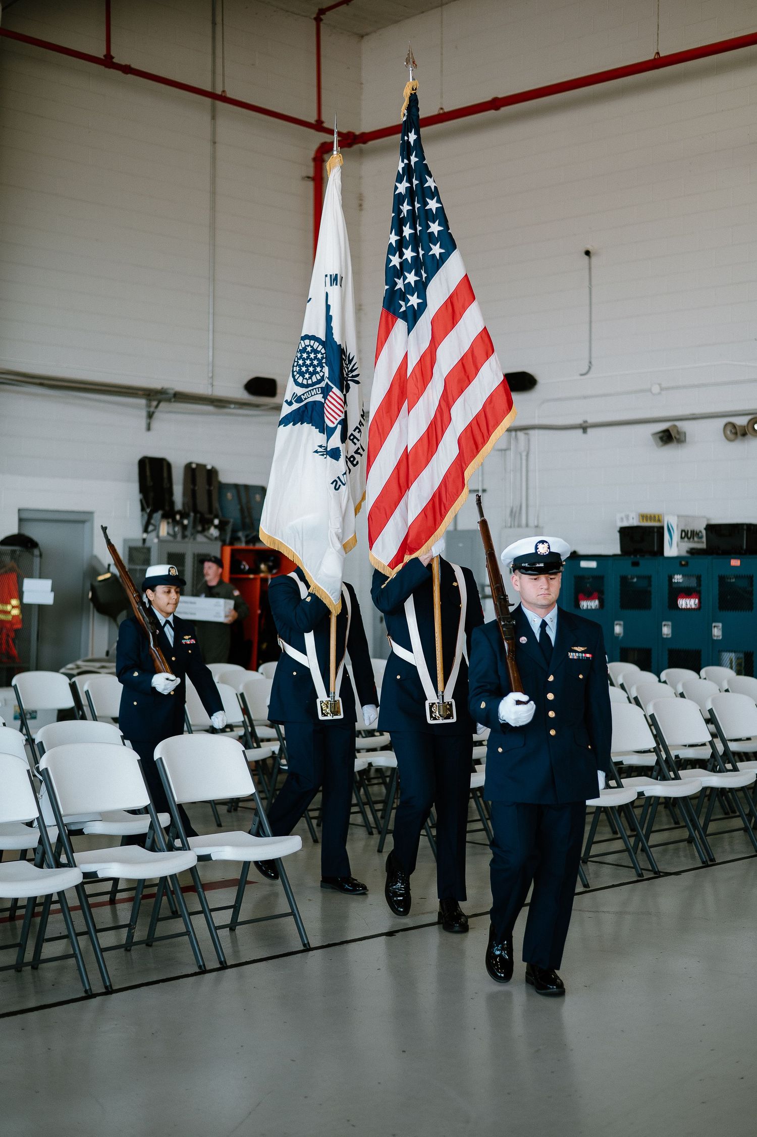 Military color guard members holding American flags stand in formation during a formal ceremony.