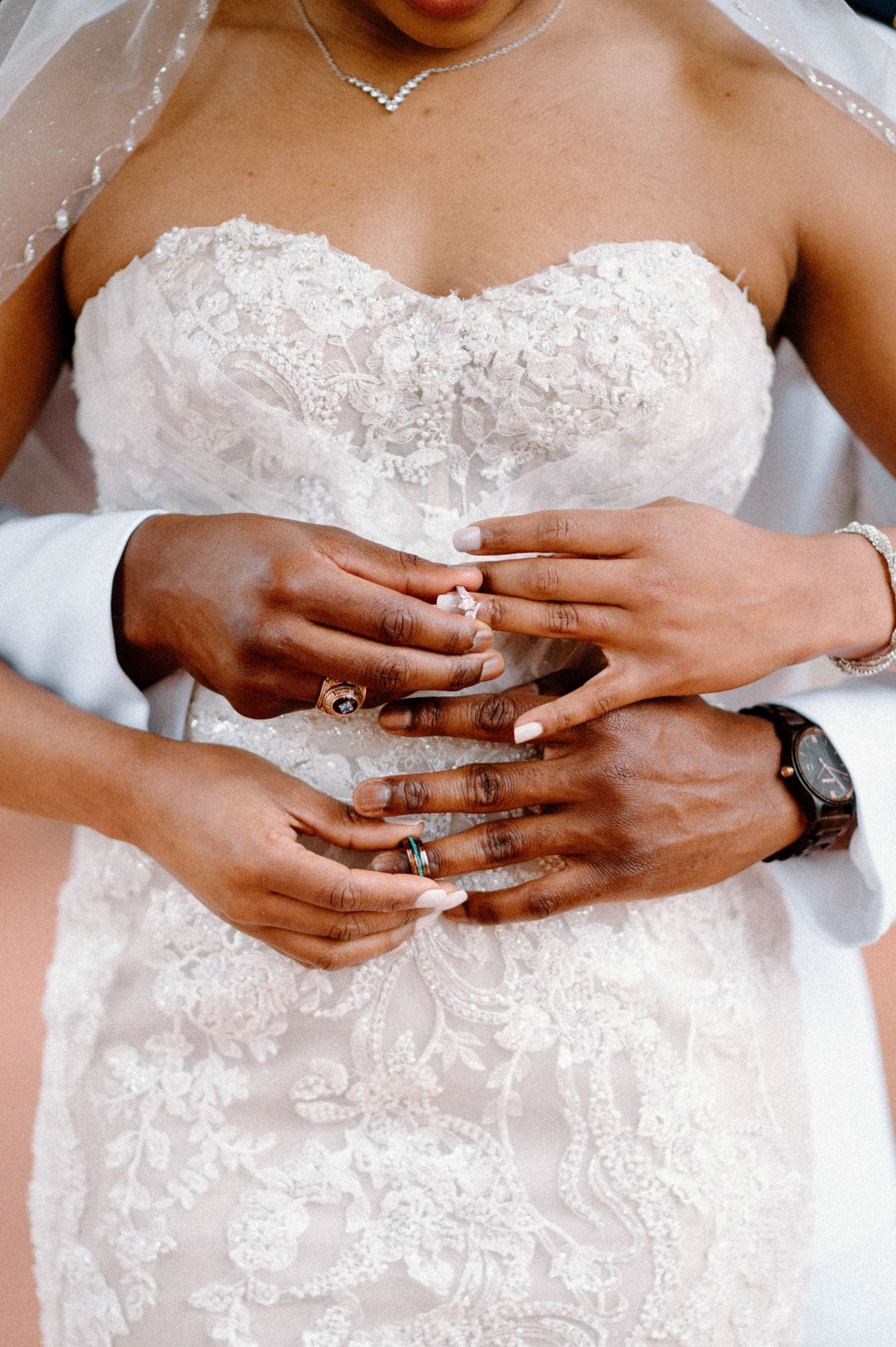 Close-up shots of hands wearing wedding rings against white lace dress.