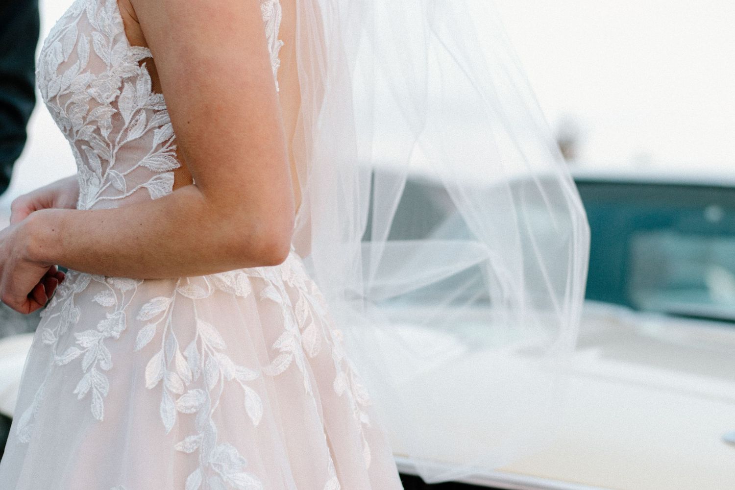 Detail shot of delicate lace wedding dress against white background.