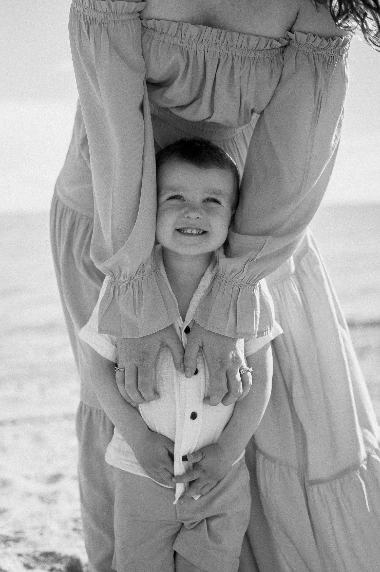 Black and white photo of parent and child playing peek-a-boo in matching outfits.