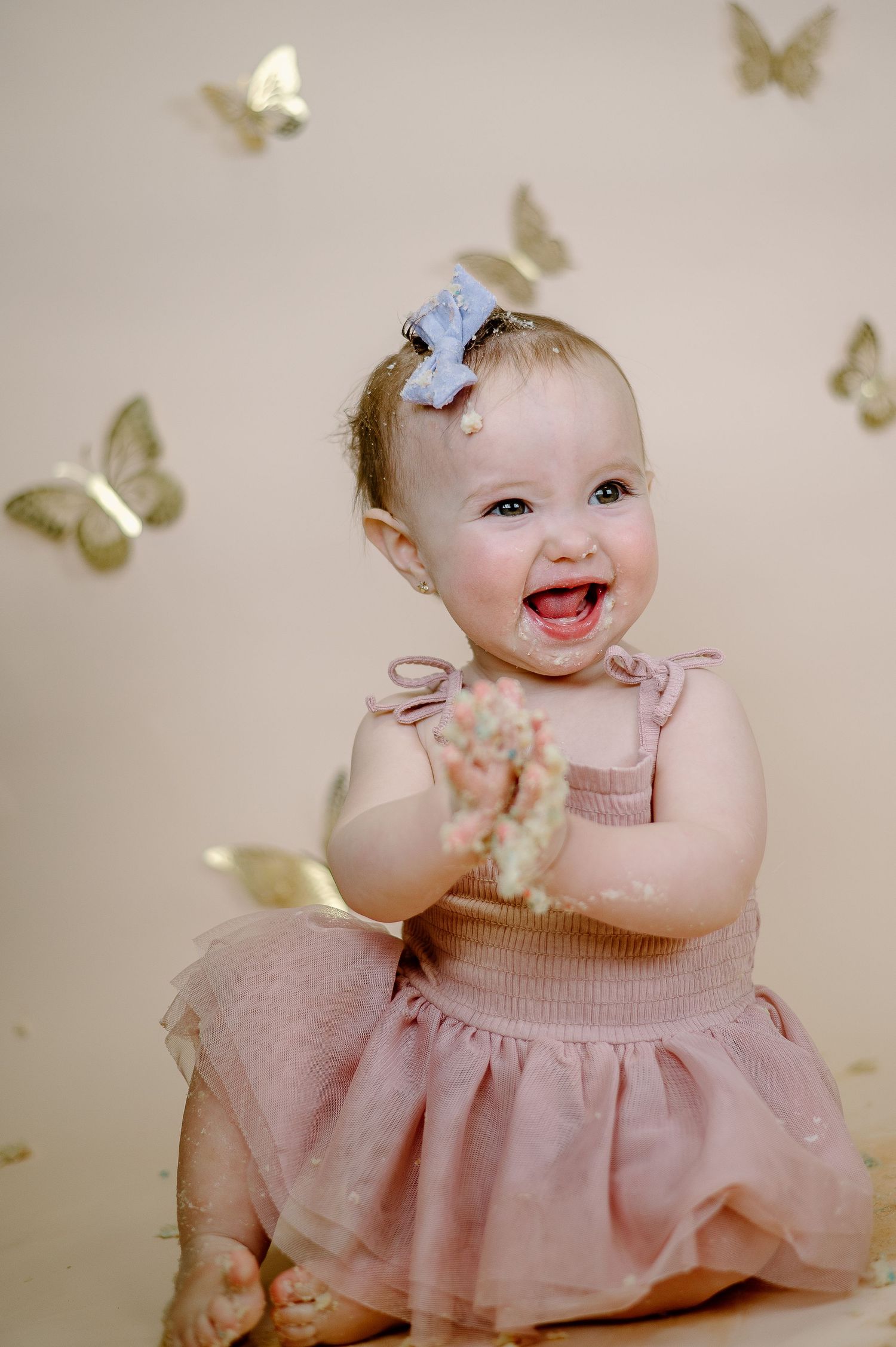 Baby wearing pink tulle dress smiles joyfully surrounded by gold butterfly decorations.