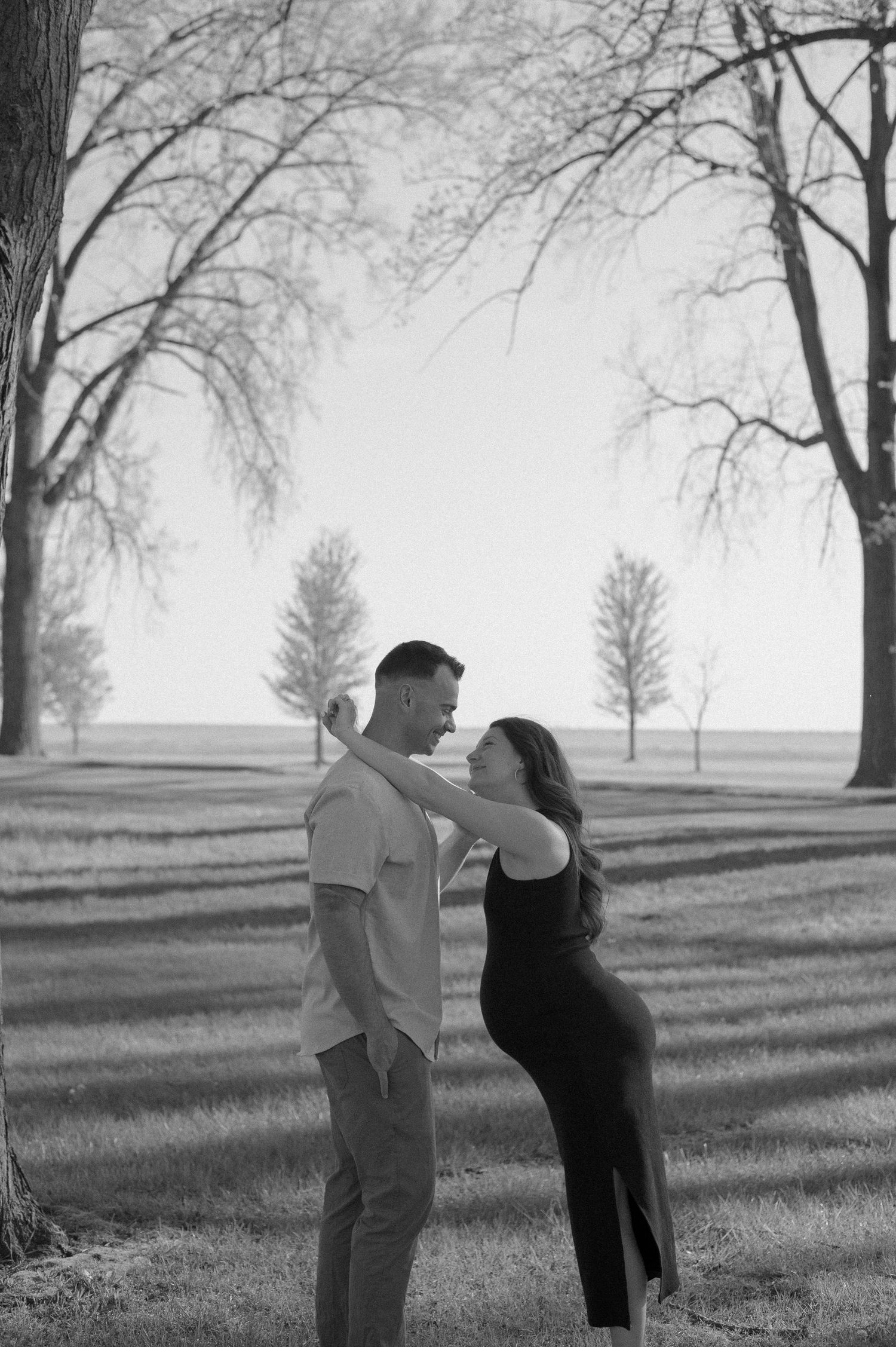 Black and white maternity photo series showing couple in a peaceful outdoor setting with bare trees.