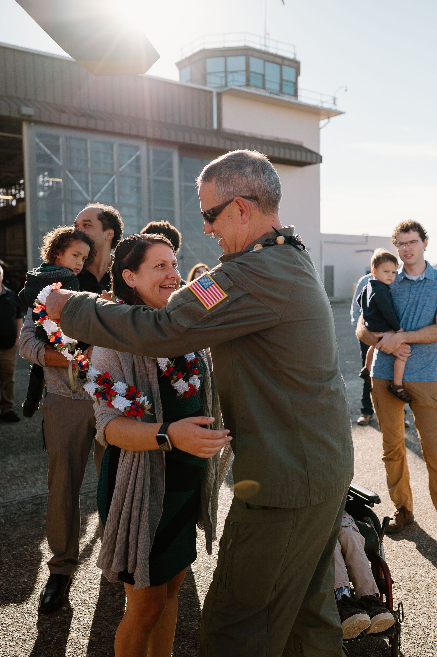 Military officer placing a floral lei on a smiling woman at an airbase homecoming celebration.