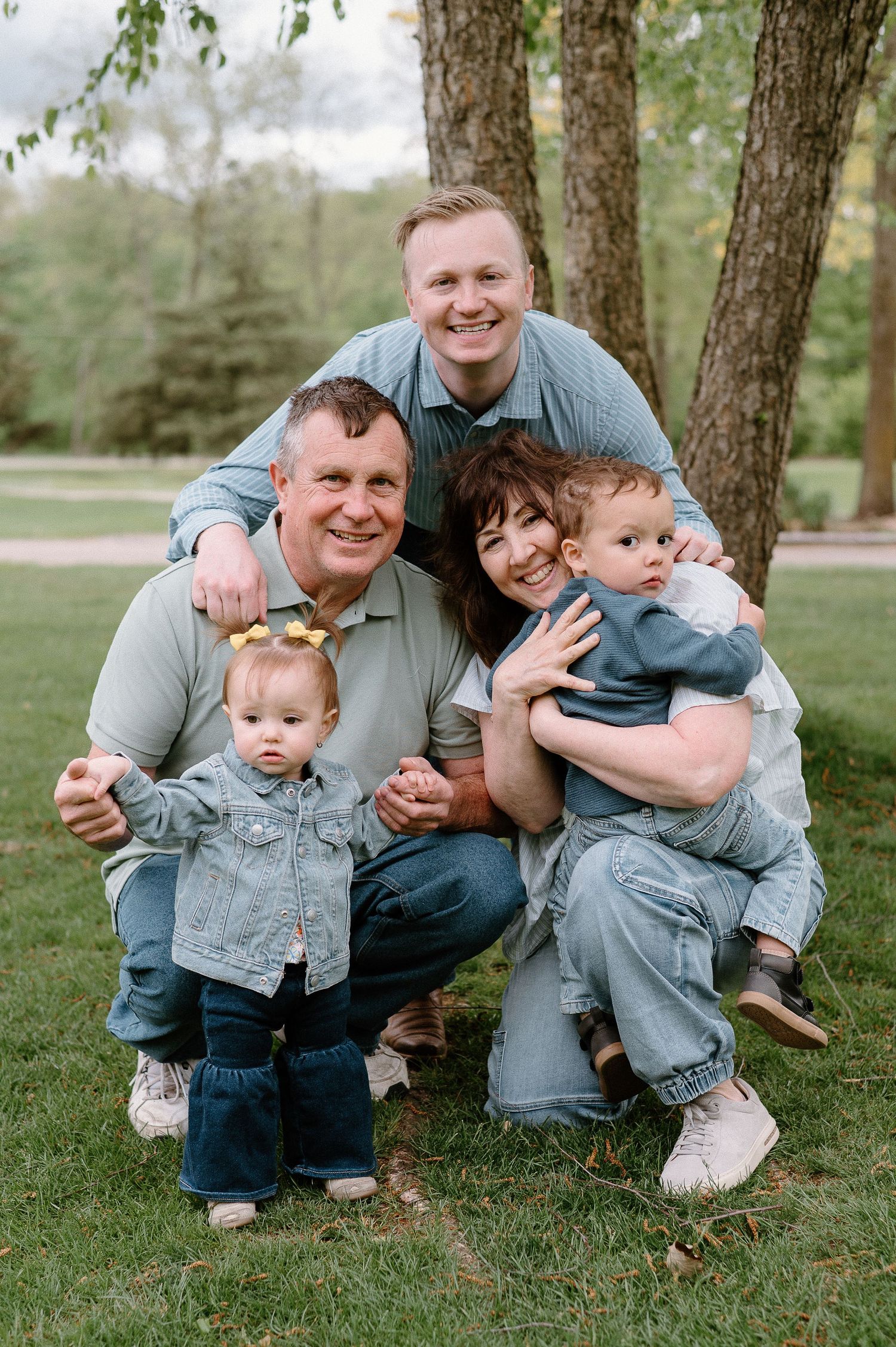 A multigenerational family group poses together outdoors on a grassy lawn.